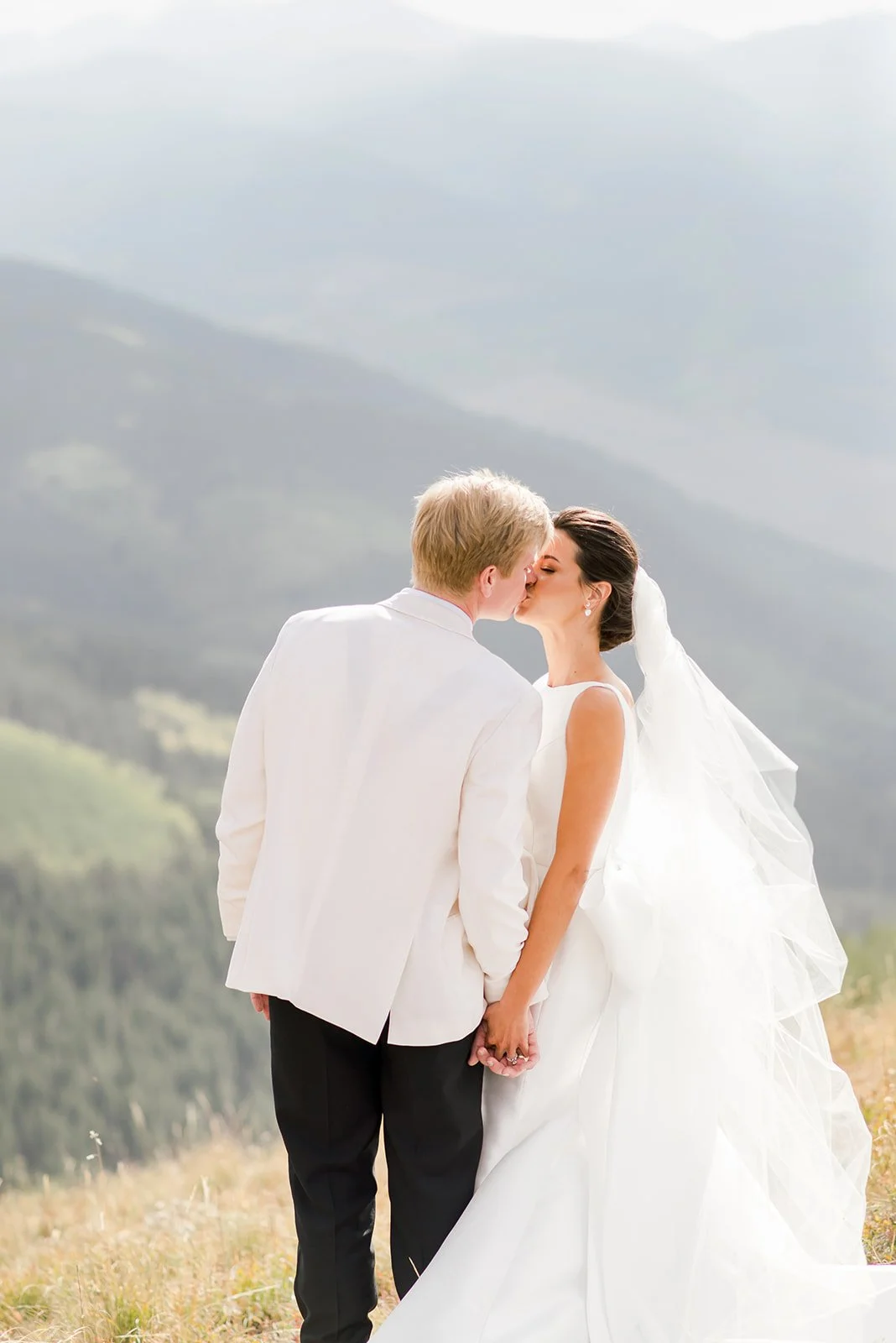 Bride and groom kissing on a mountaintop overlooking the Vail Valley.