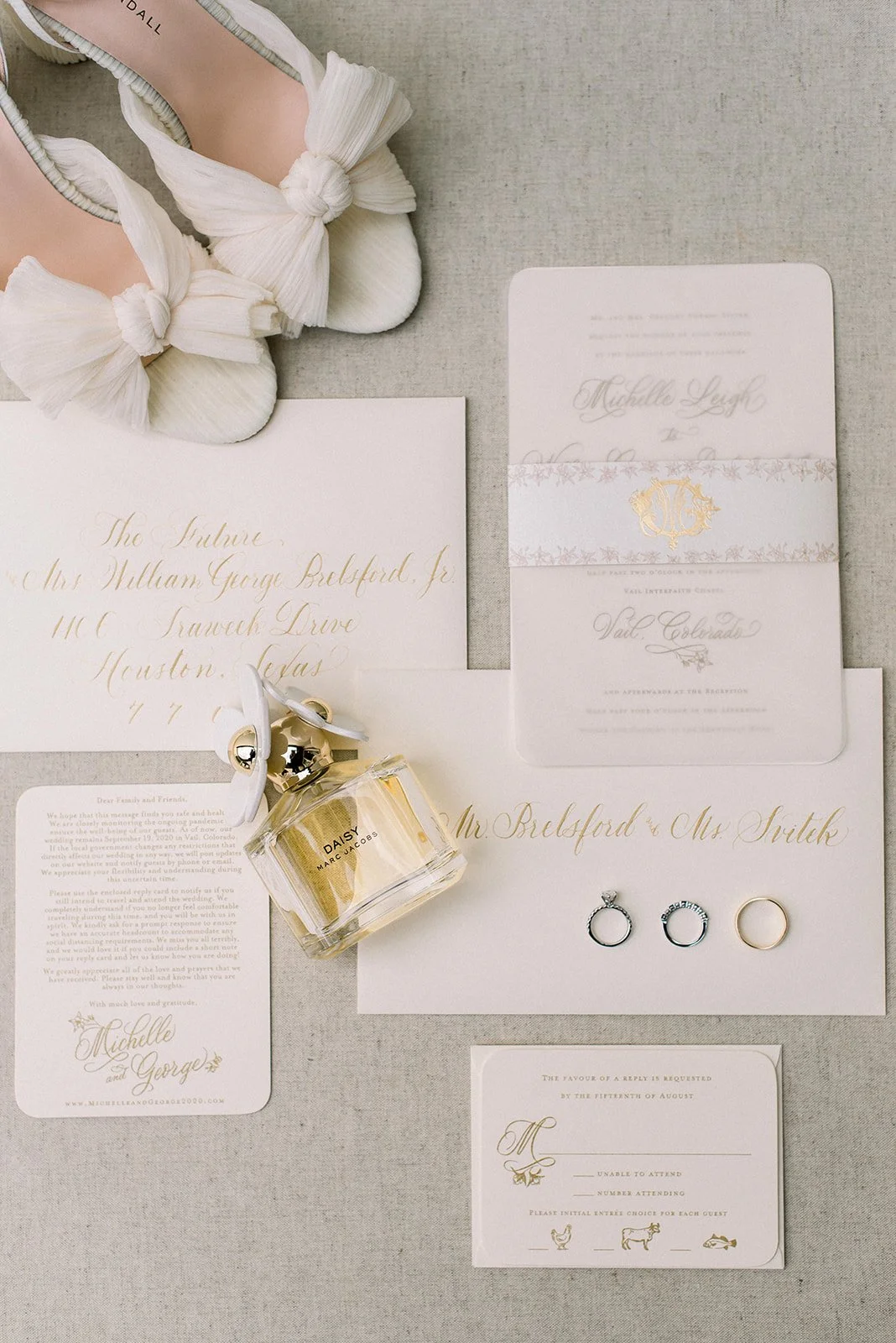 White and gold wedding stationery, rings and perfume arranged for a Vail wedding.