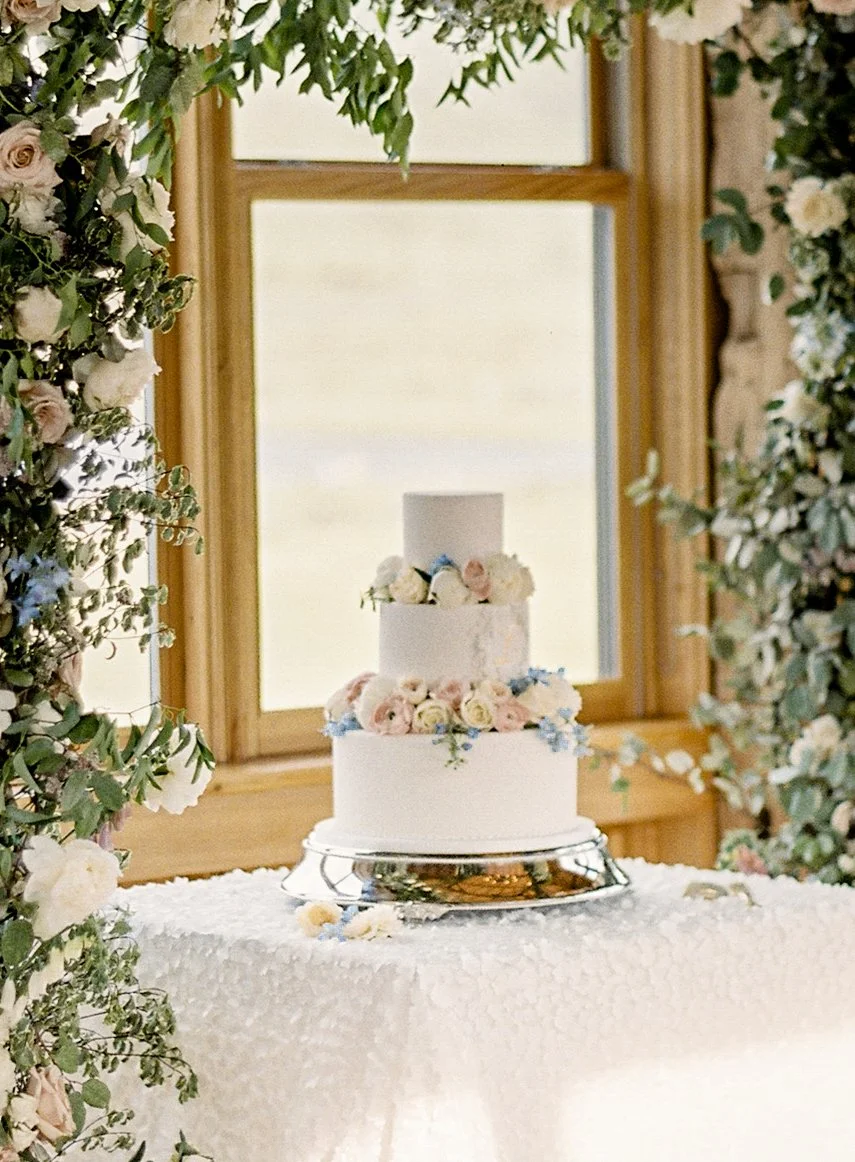 A classic wedding cake under a floral arch at Devil's Thumb Ranch