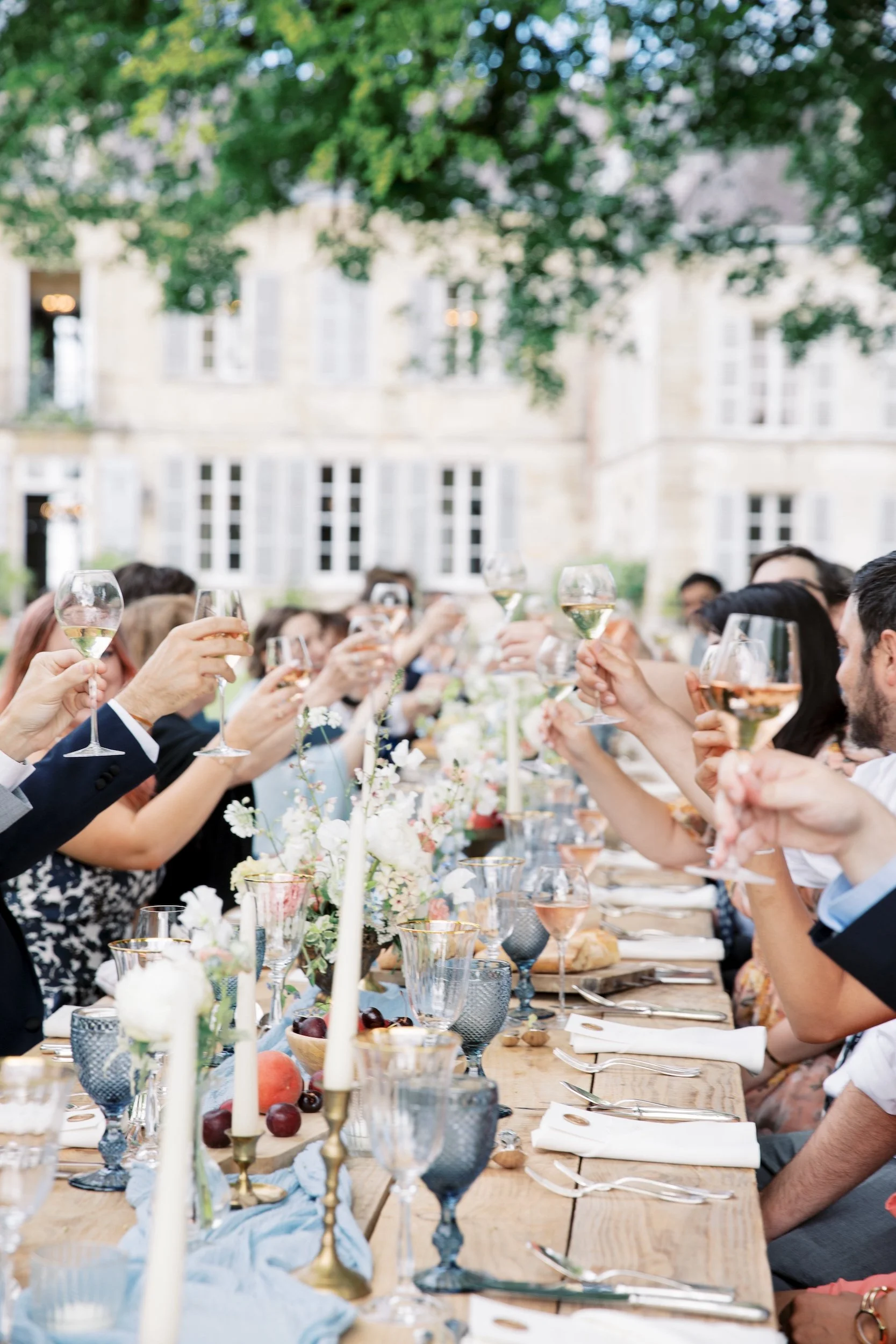 Guests raising their glasses around a long outdoor wedding dinner table