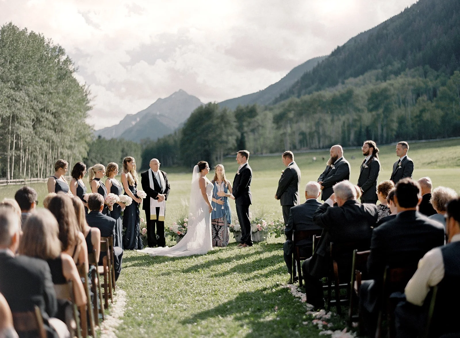Outdoor wedding ceremony in the Colorado mountains with guests seated overlooking a meadow and mountain backdrop. Venue T-Lazy-7 Ranch, photo by Alp & Isle Photography