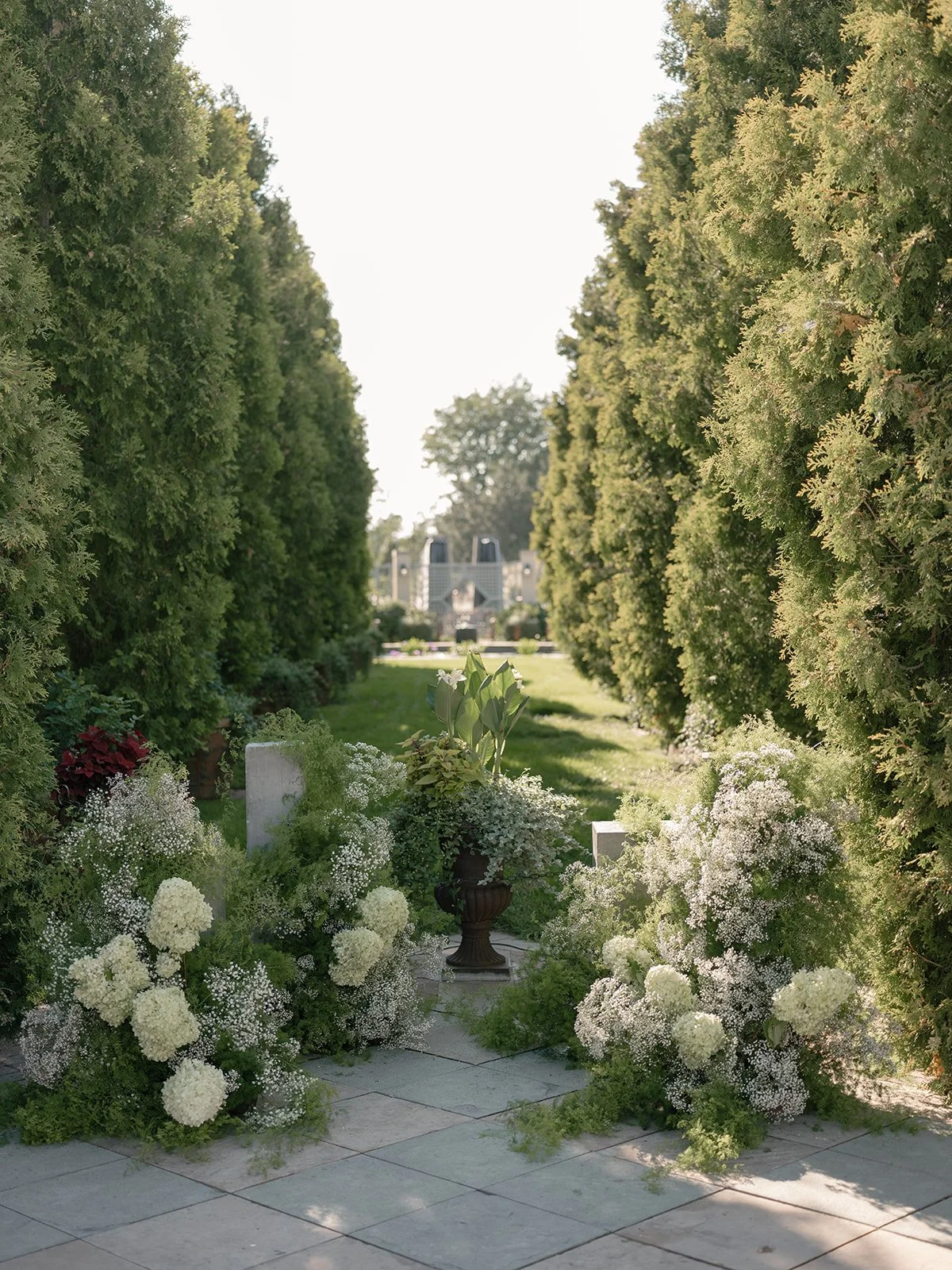 A manicured garden walkway lined with abundant greenery and white florals, designed for a romantic outdoor wedding at the Denver Botanic Gardens. Photo by Kelli Christine Photography.