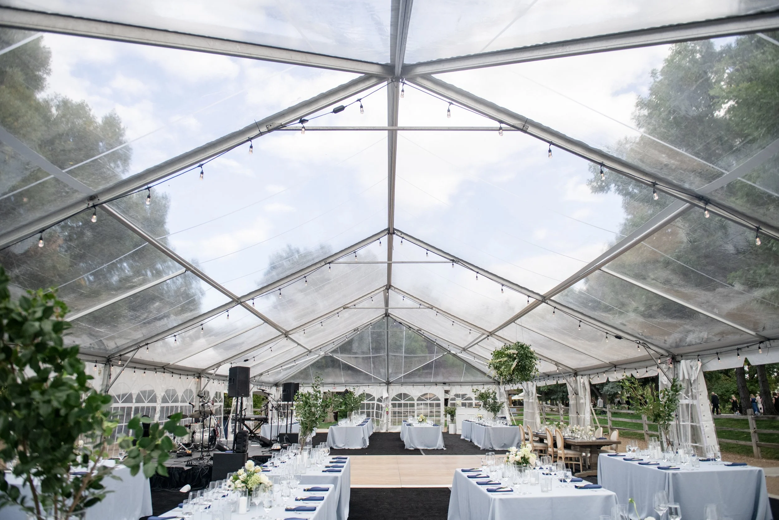 Interior view of a luxury wedding tent showing flooring, dining tables, lighting, and event infrastructure required for a fully built reception.