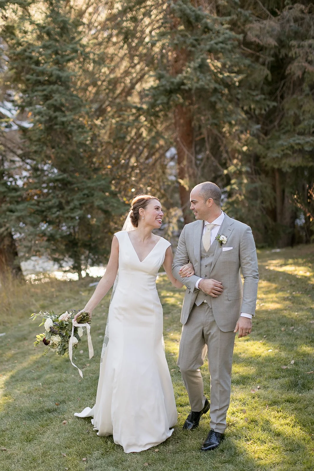 C and J walking together after their wedding ceremony in Vail, Colorado, surrounded by evergreen trees.
