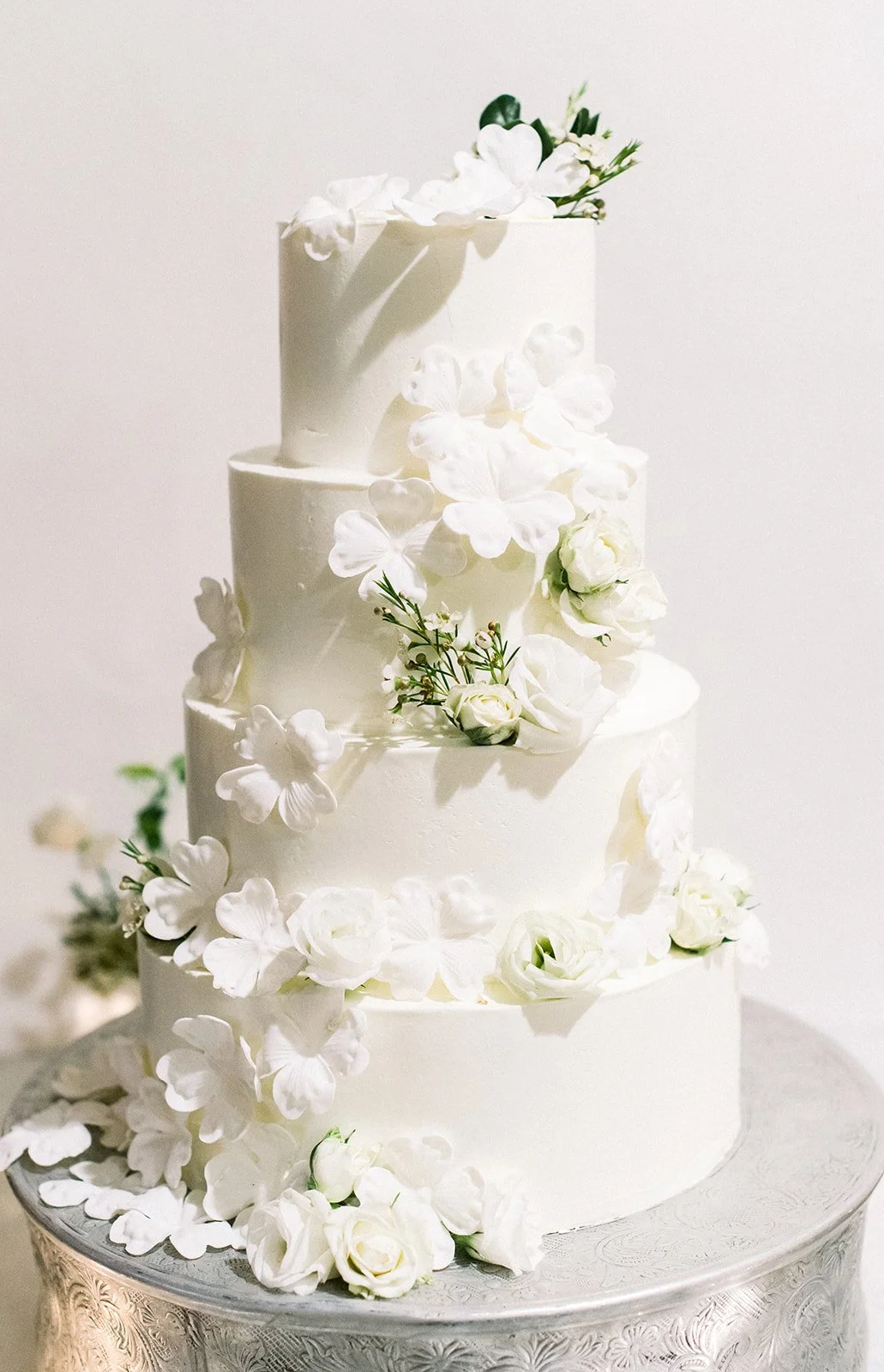 Tiered white wedding cake decorated with white sugar flowers and greenery.