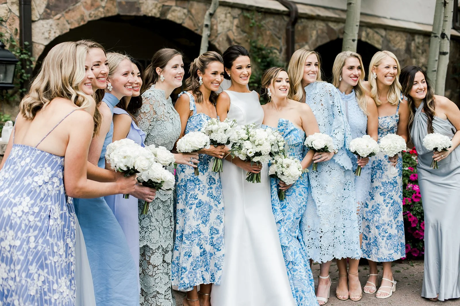 A bride photographed with her bridesmaids in coordinated, mix-and-match pattern blue dresses, holding white bouquets at The Sonnenalp in Vail, Colorado. Photo by Rachel Schrepel.