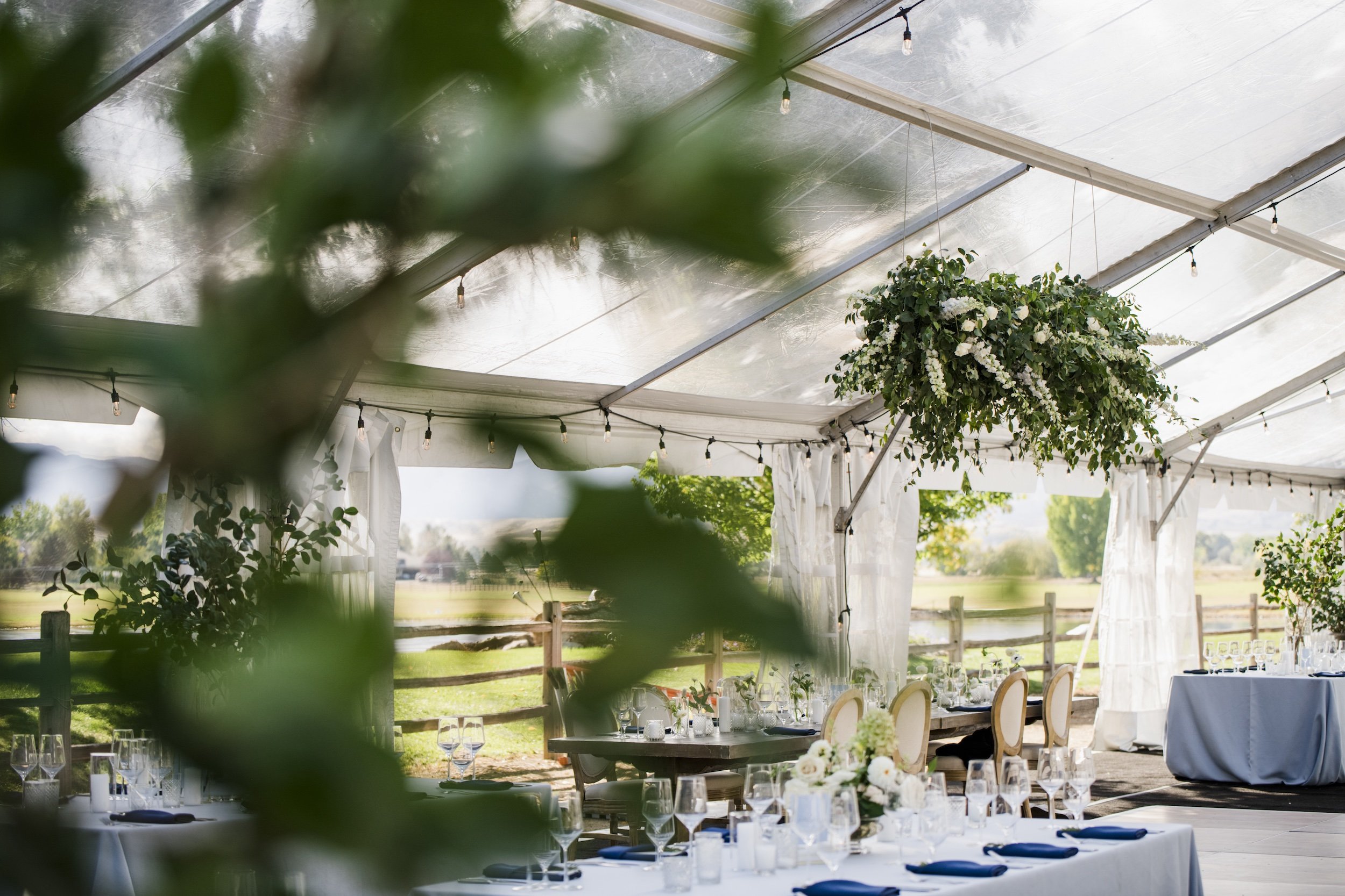 Clear-top wedding tent and reception tables framed by lush greenery