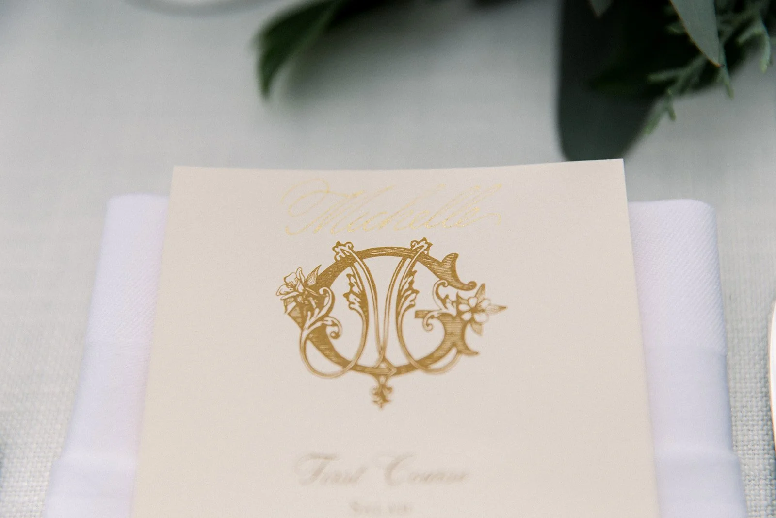 Gold monogrammed wedding menu resting on a folded white napkin.