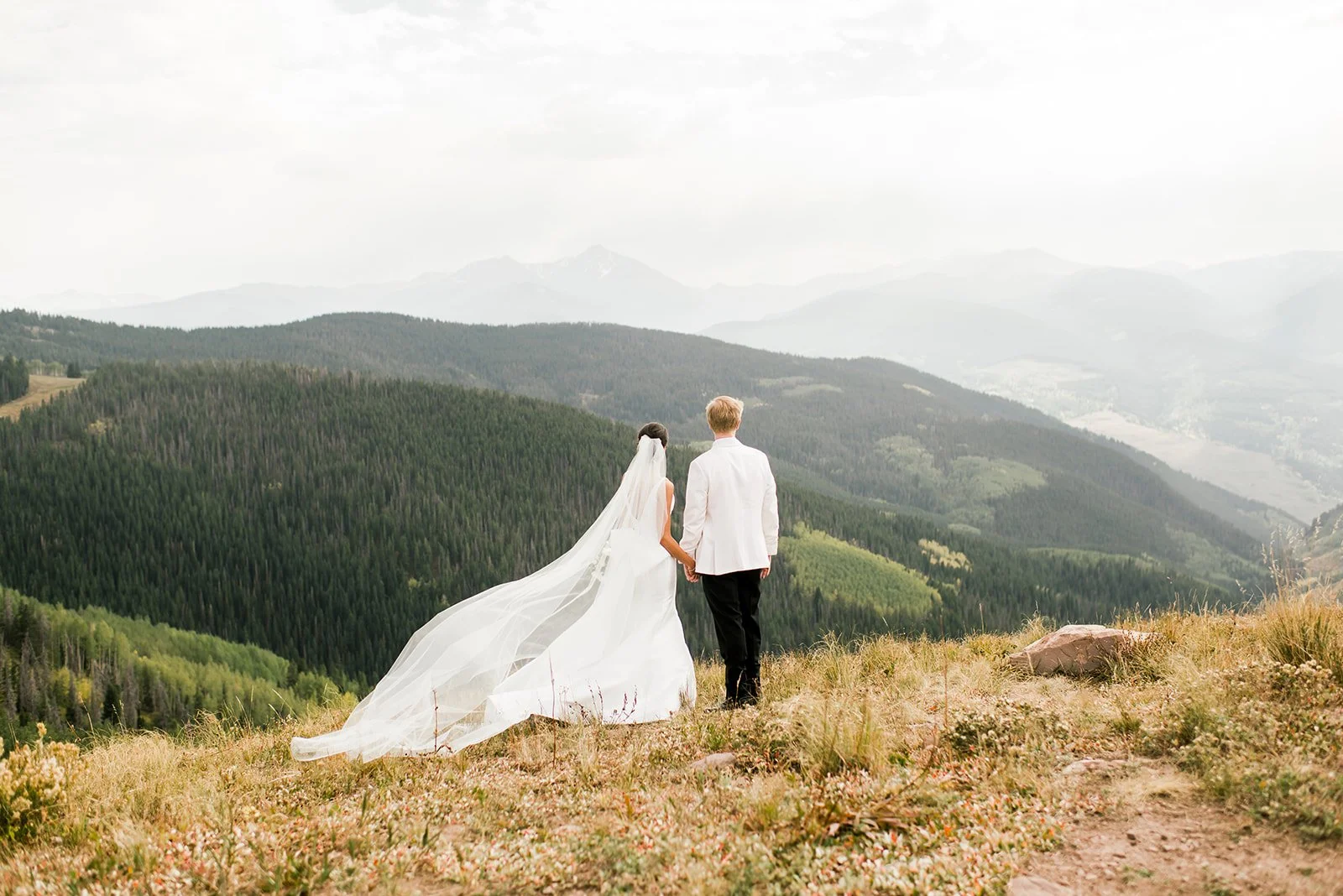 Wide portrait of newlyweds overlooking layered mountain ridges in Vail.