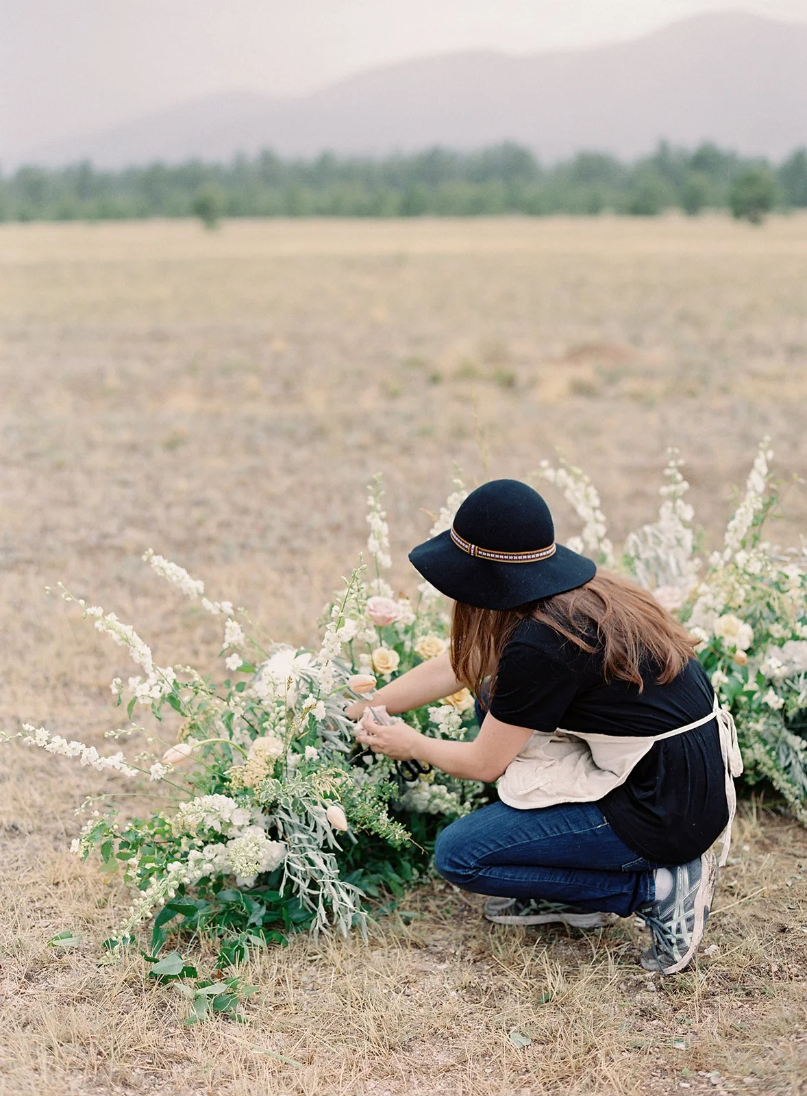 A florist arranging ceremony florals outdoors before a wedding, illustrating behind-the-scenes preparation and planning required for a luxury event.
