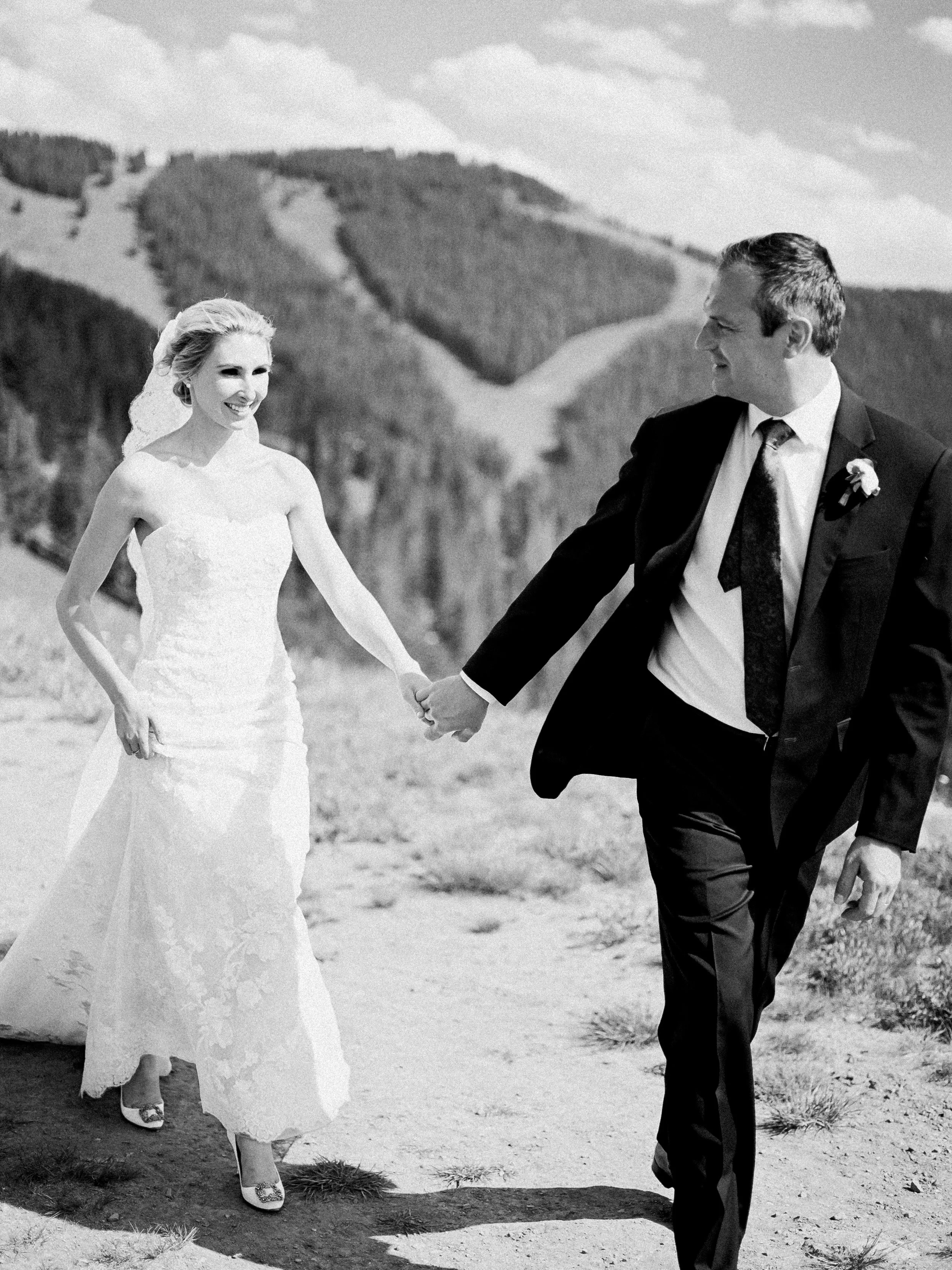 Bride and groom holding hands with forested mountain slopes behind them during a wedding in Vail, Colorado.