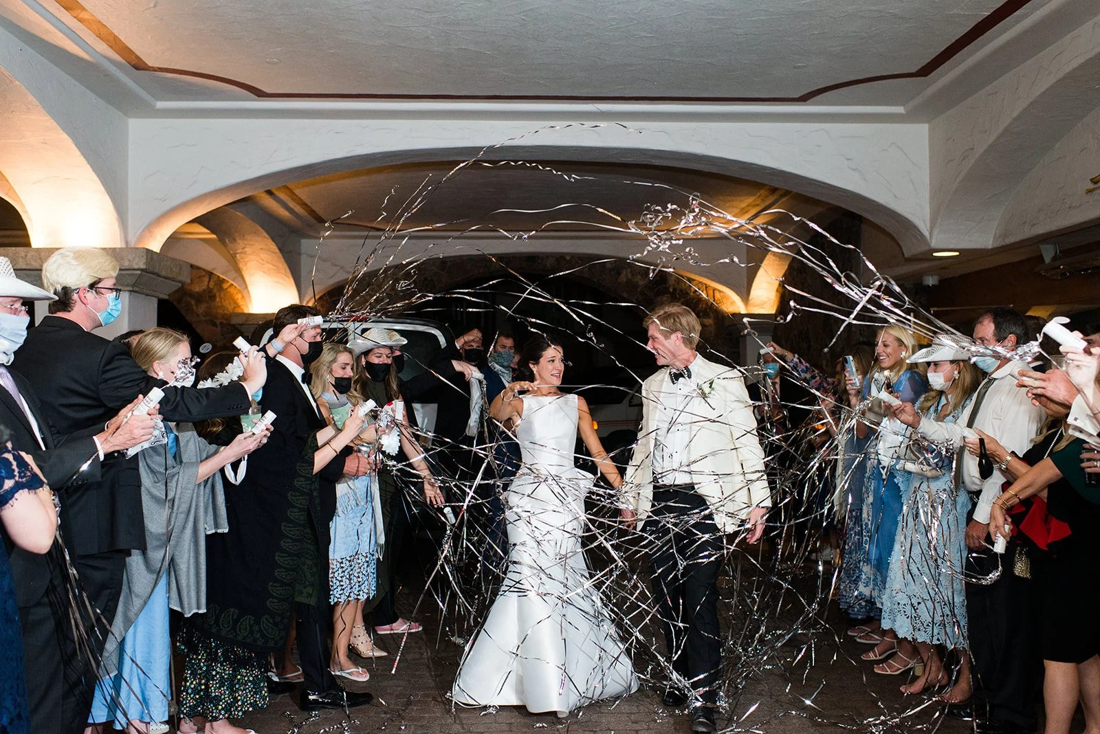 Newlyweds walking through a streamer-filled reception exit surrounded by guests.