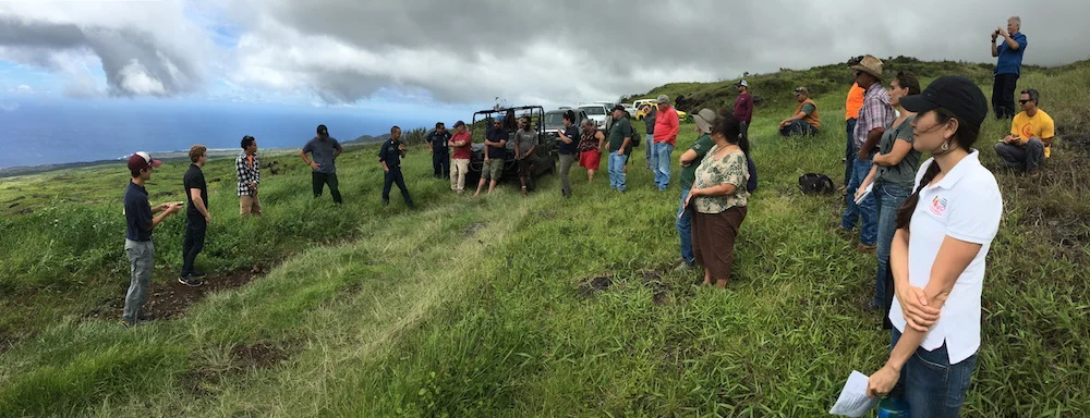 Firefighters share their experiences fighting fires in Kahikinui. Attendees listen in as they survey the land from the mauka edge of the fire. Photo Credit: Clay Trauernicht/PFX
