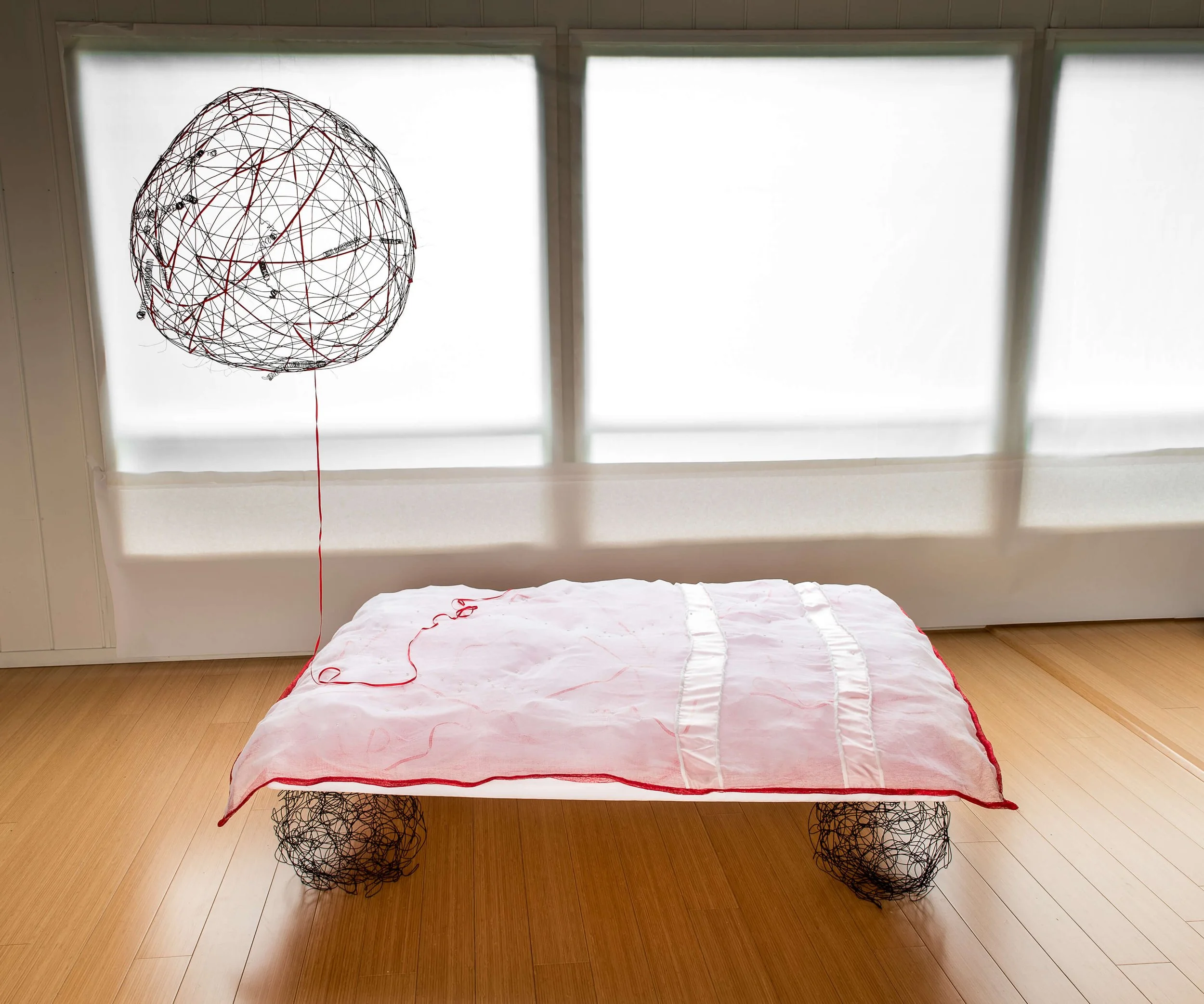MATRIMONIAL BED WITH SHARED GALAXY: Coverlet/Mattress: Cotton butter cloth, habotai silk top, tulle batt, ribbon, ‘pearls,’ red poly spider writing backing, hand sewn. Box Spring: Styrofoam support, nylon cover. Spherical ‘legs’: rebar tie wire. 58” 