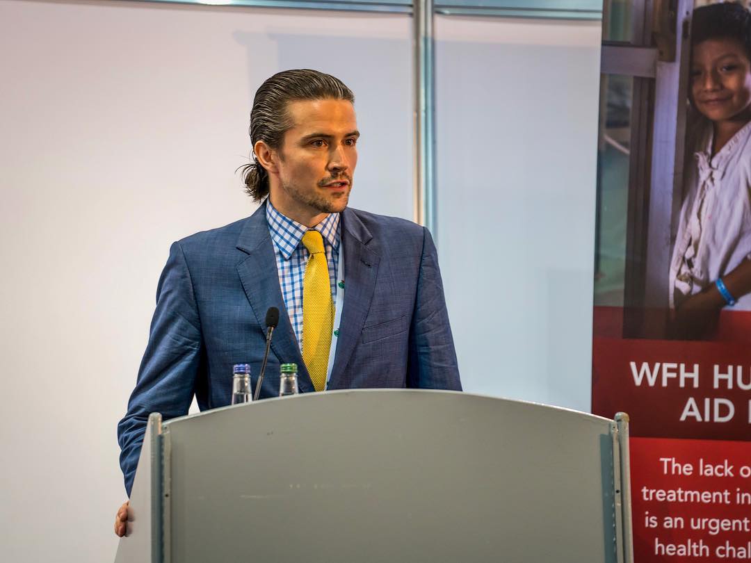 Man_In_Suit_Standing_At_A_Podium.jpg