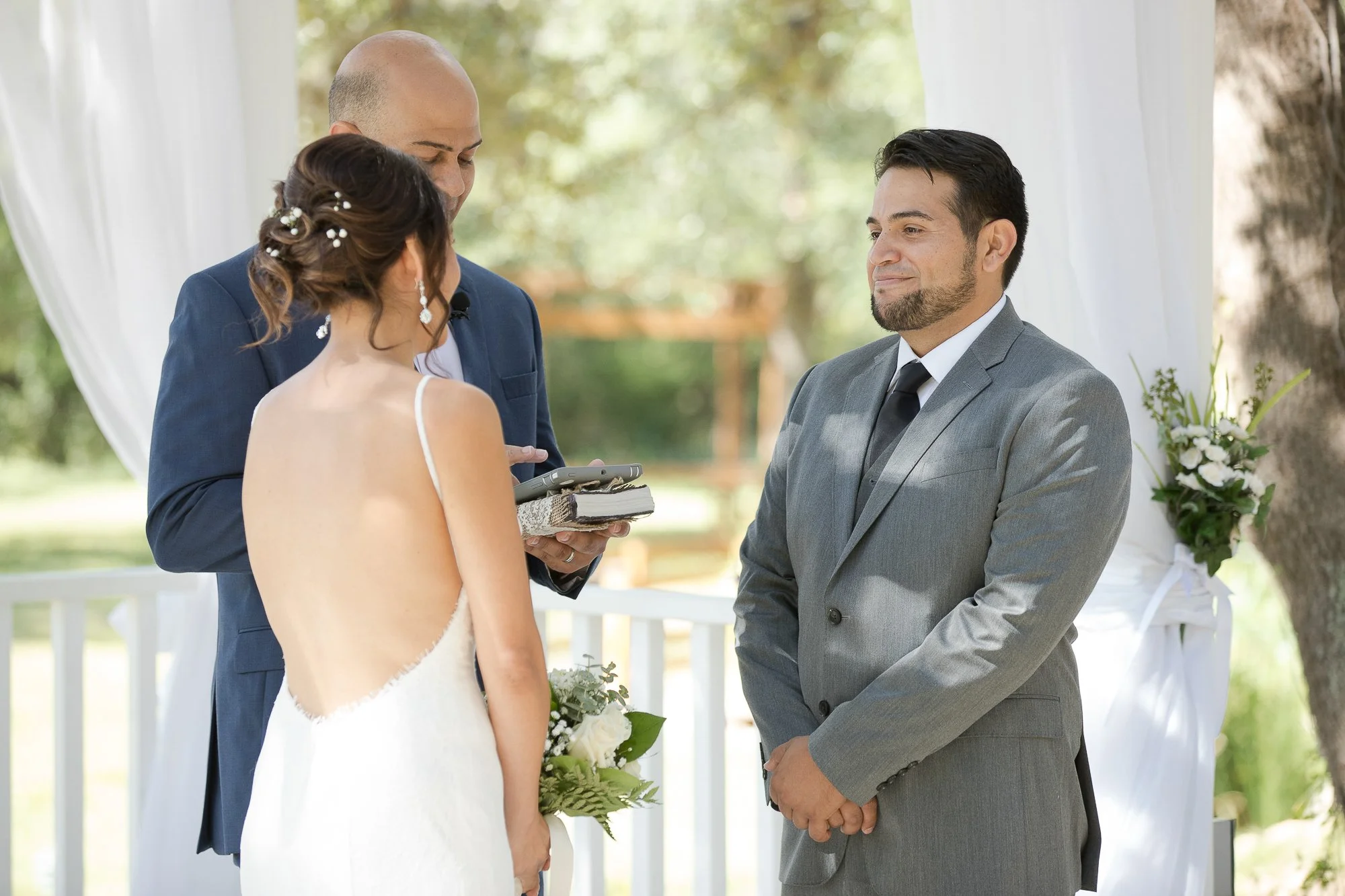 Bride and groom exchanging vows during outdoor wedding ceremony, officiant standing behind them.