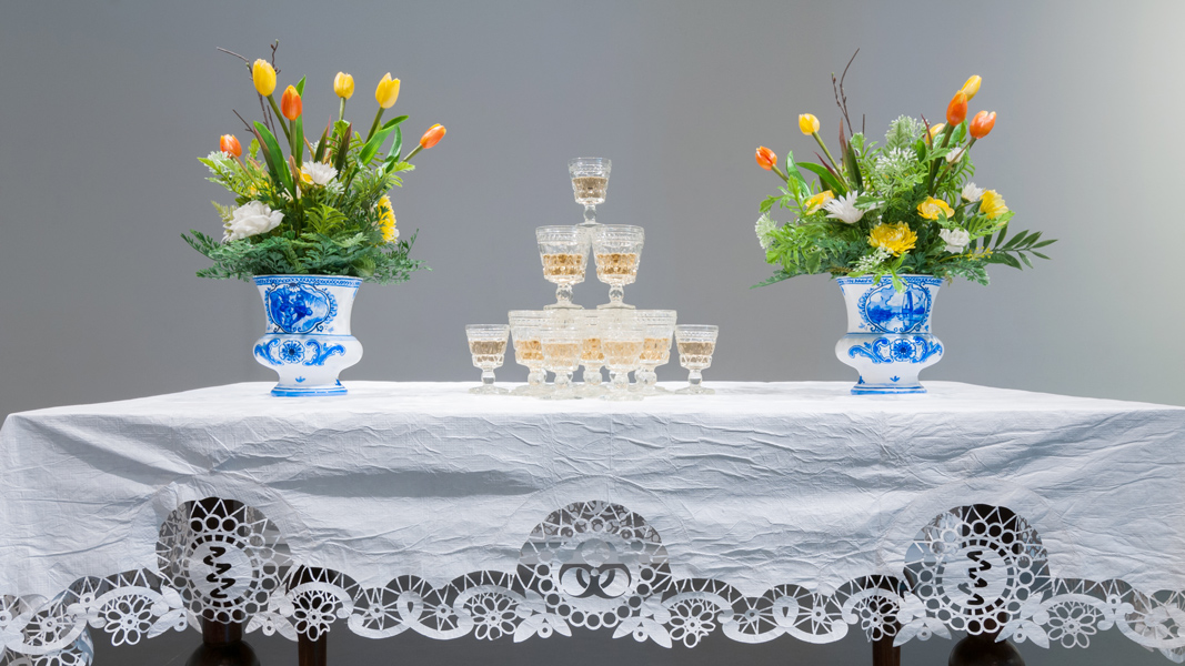   Drink  (detail), 2016 Brass chandelier with fruit-bat crystals, 17th century-Dutch-style table, Tyvek® table cloth, stemware with wine, hand-painted Delftware-style vases with plastic flowers imensions variable 