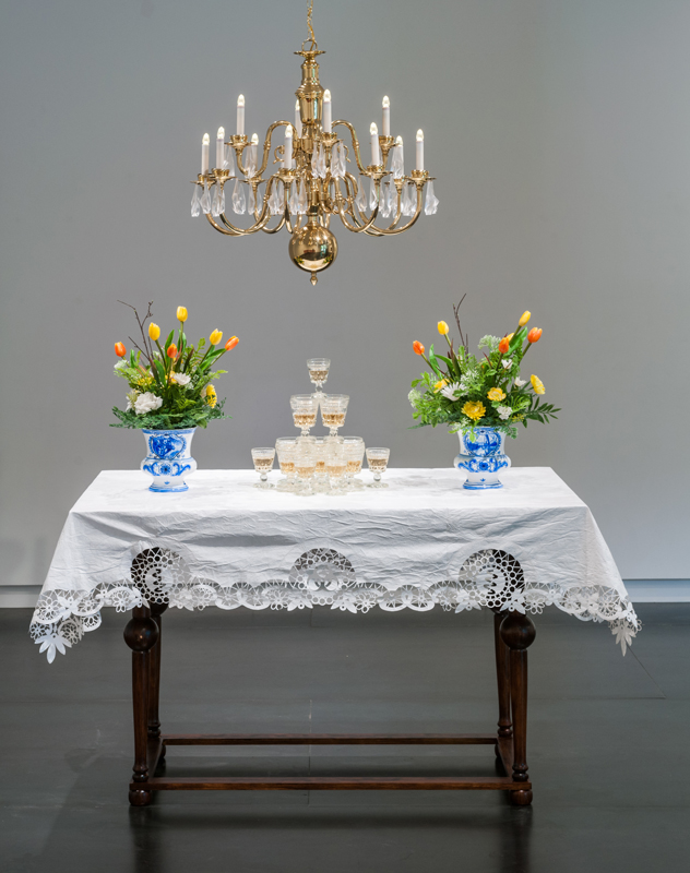   Drink , 2016 Brass chandelier with fruit-bat crystals, 17th century-Dutch-style table, Tyvek® table cloth, stemware with wine, hand-painted Delftware-style vases with plastic flowers dimensions variable 