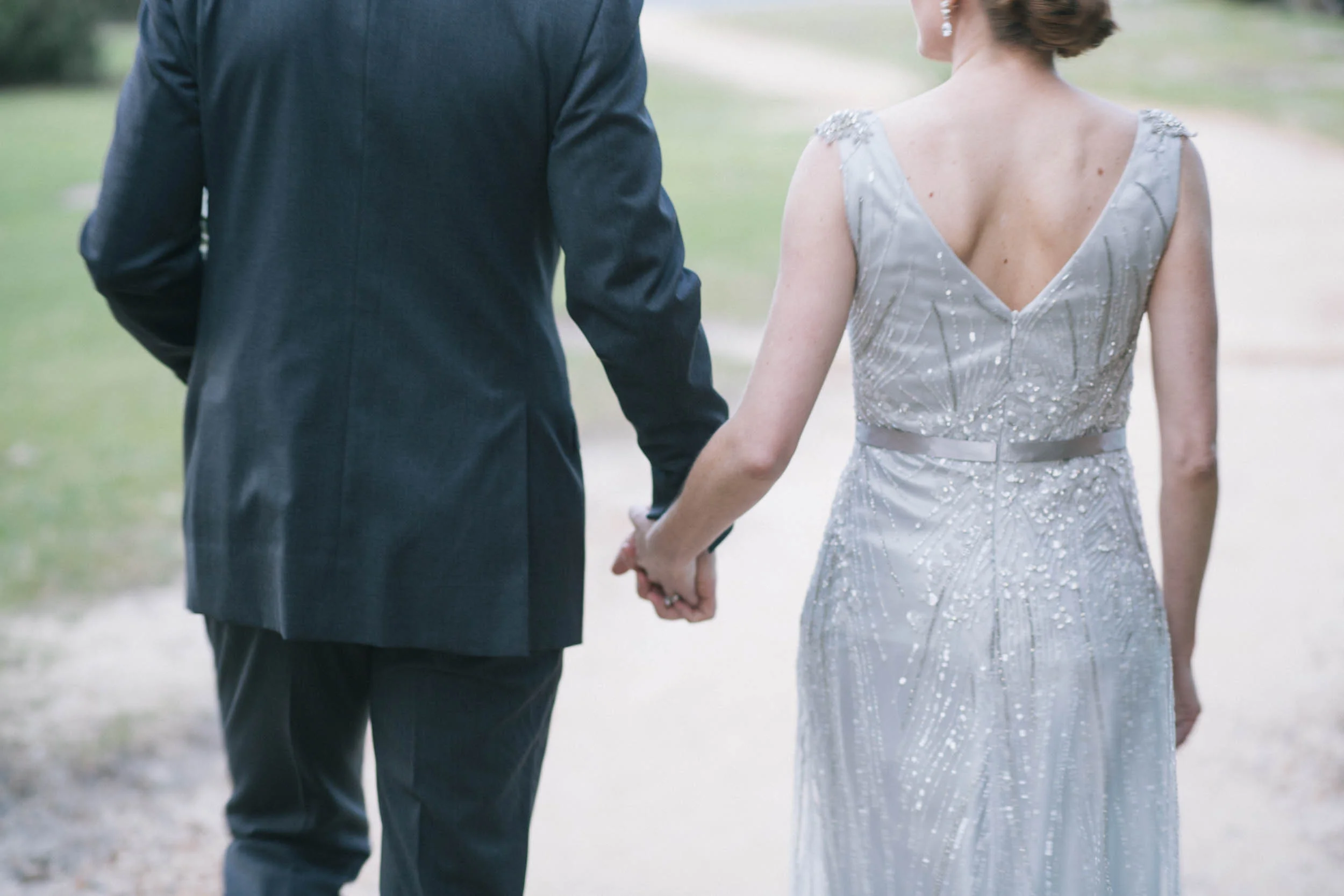 A couple holding hands, walking outdoors, with the woman wearing a sequined dress and earrings, and the man in a suit.