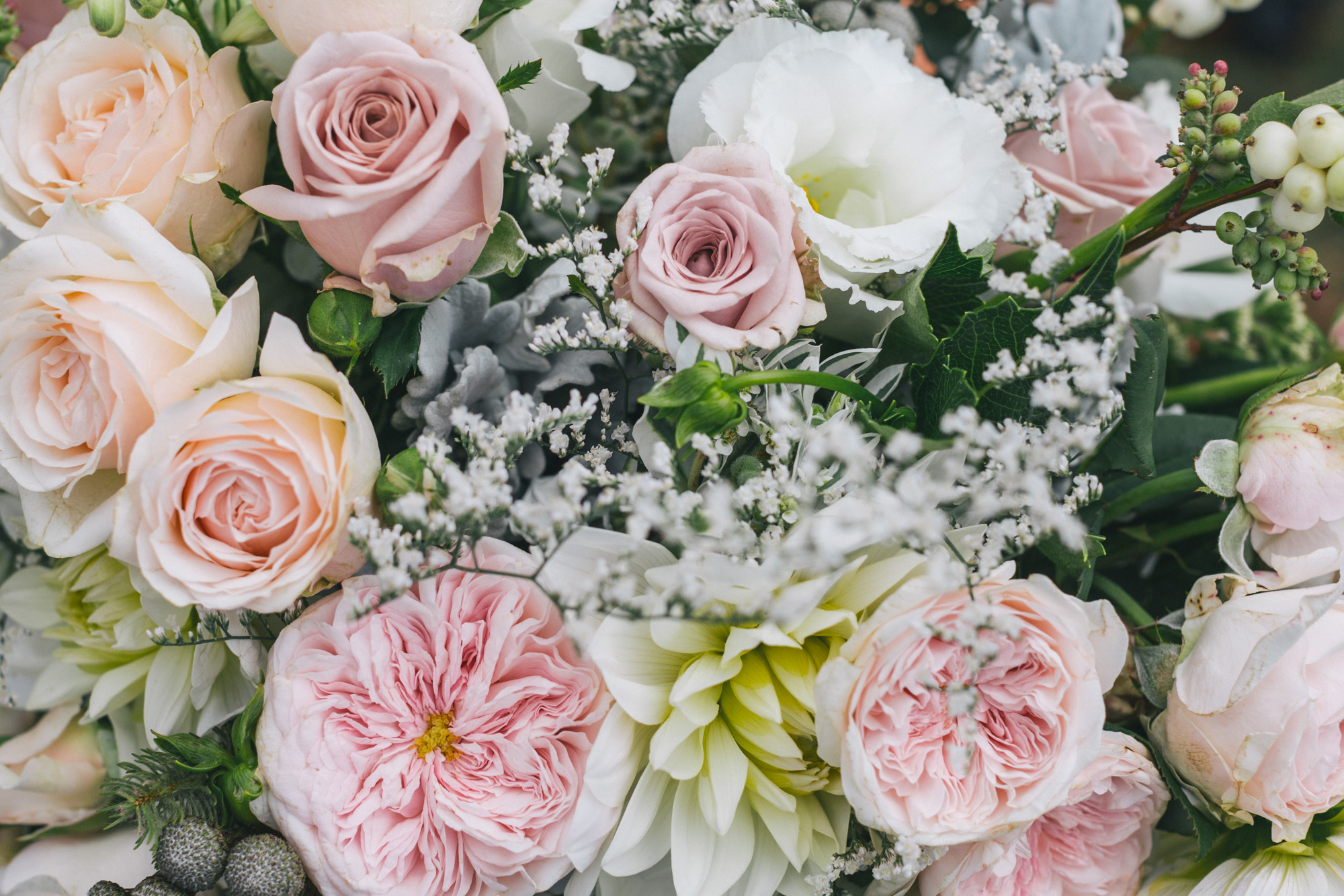 Close-up view of a bouquet of flowers featuring pale pink roses, white lilies, small white baby's breath, and green foliage.