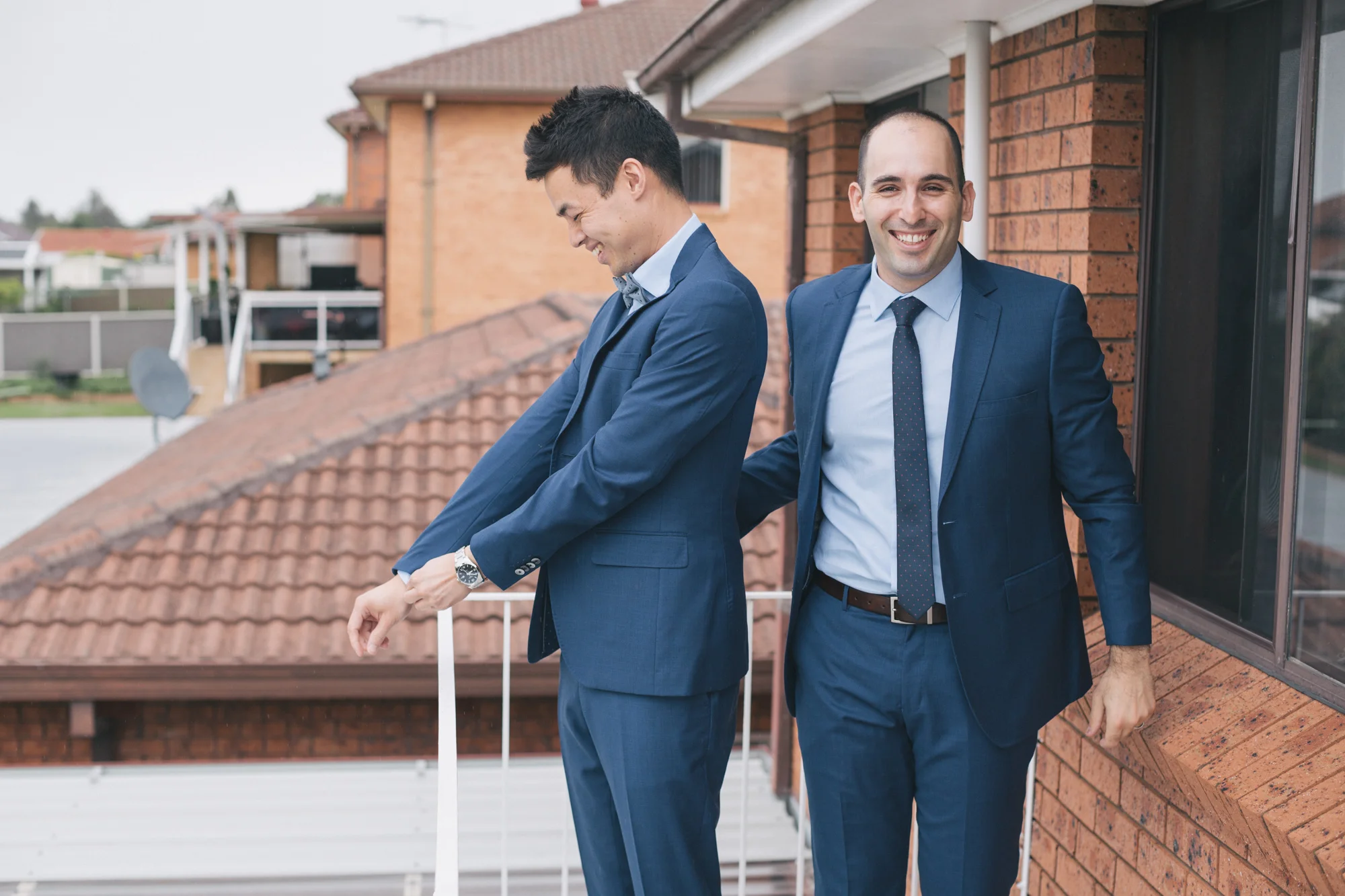 Two men in blue suits laughing outside a brick building.