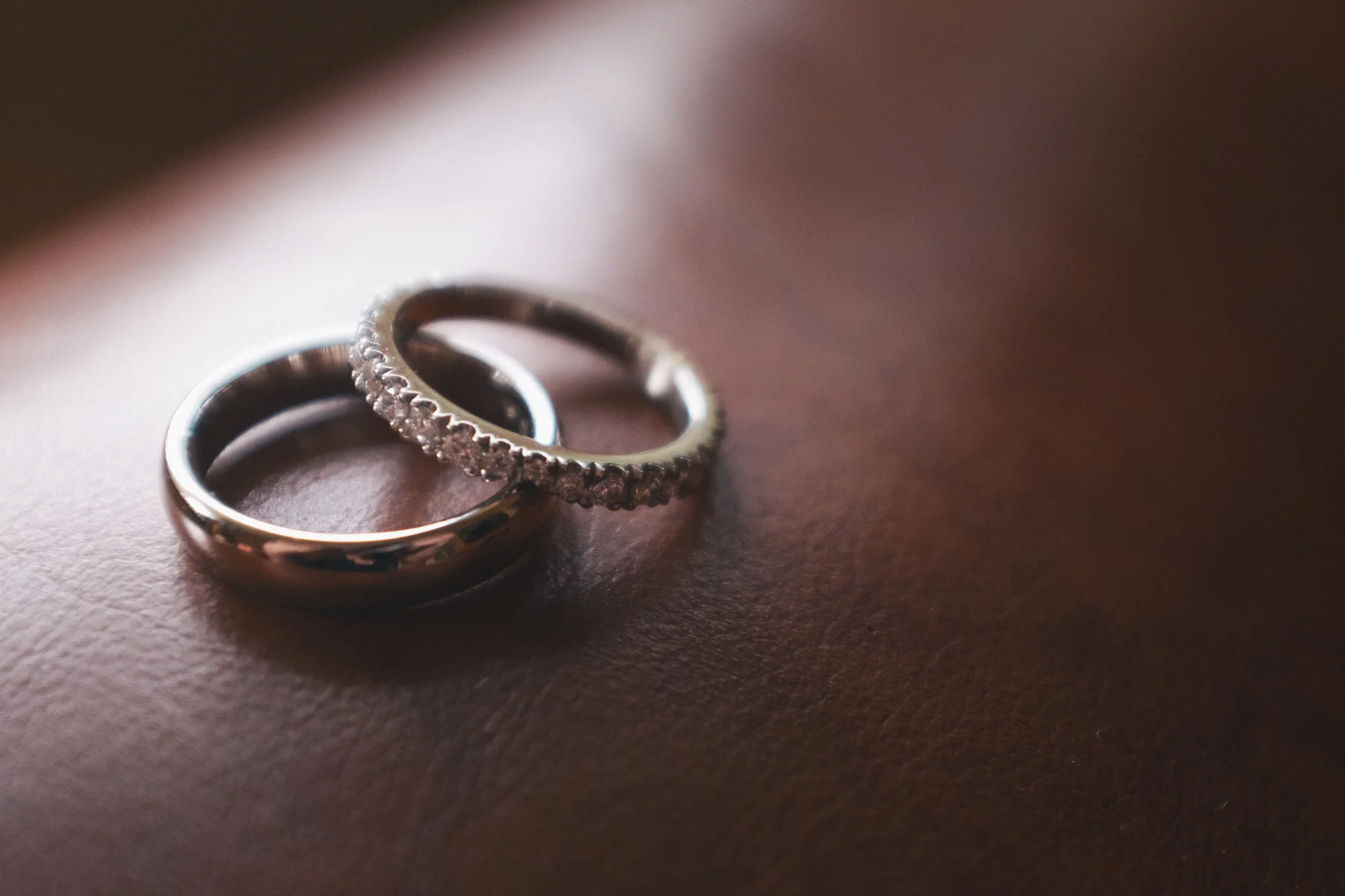 Close-up of two silver rings, one plain band and one with small embedded stones, on a pink surface.
