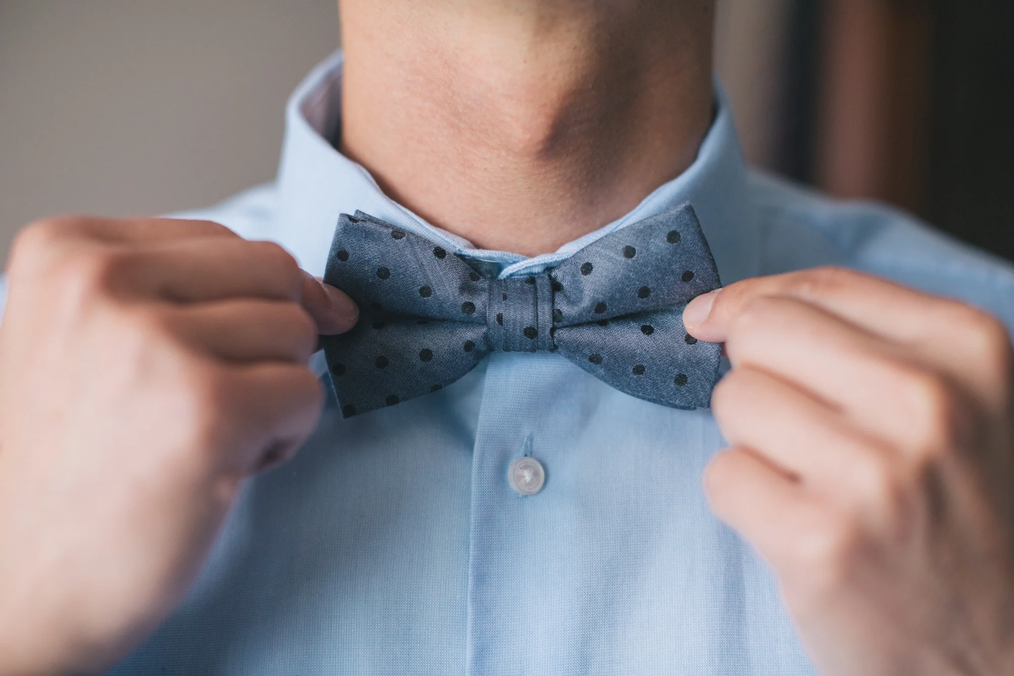 A person adjusting a polka dot bow tie on a light blue dress shirt.