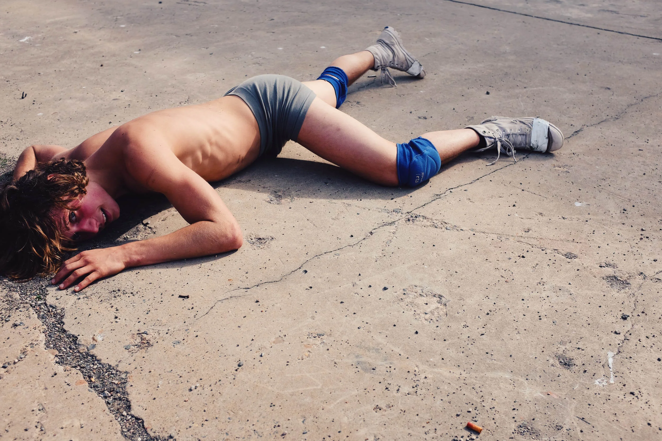 Person in athletic gear lying on concrete surface, wearing knee pads and sneakers.