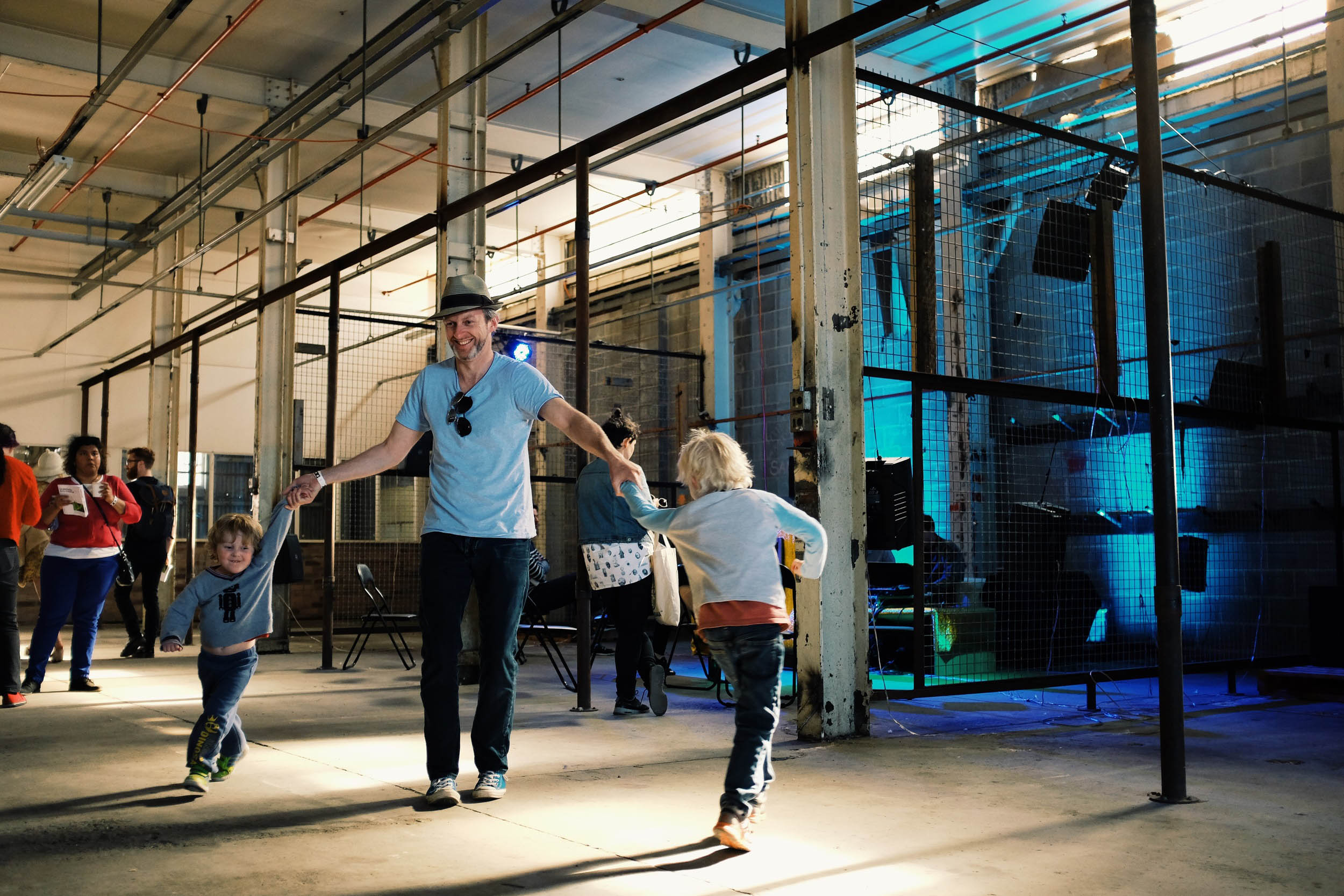 Man with hat dancing with two children in industrial-style venue