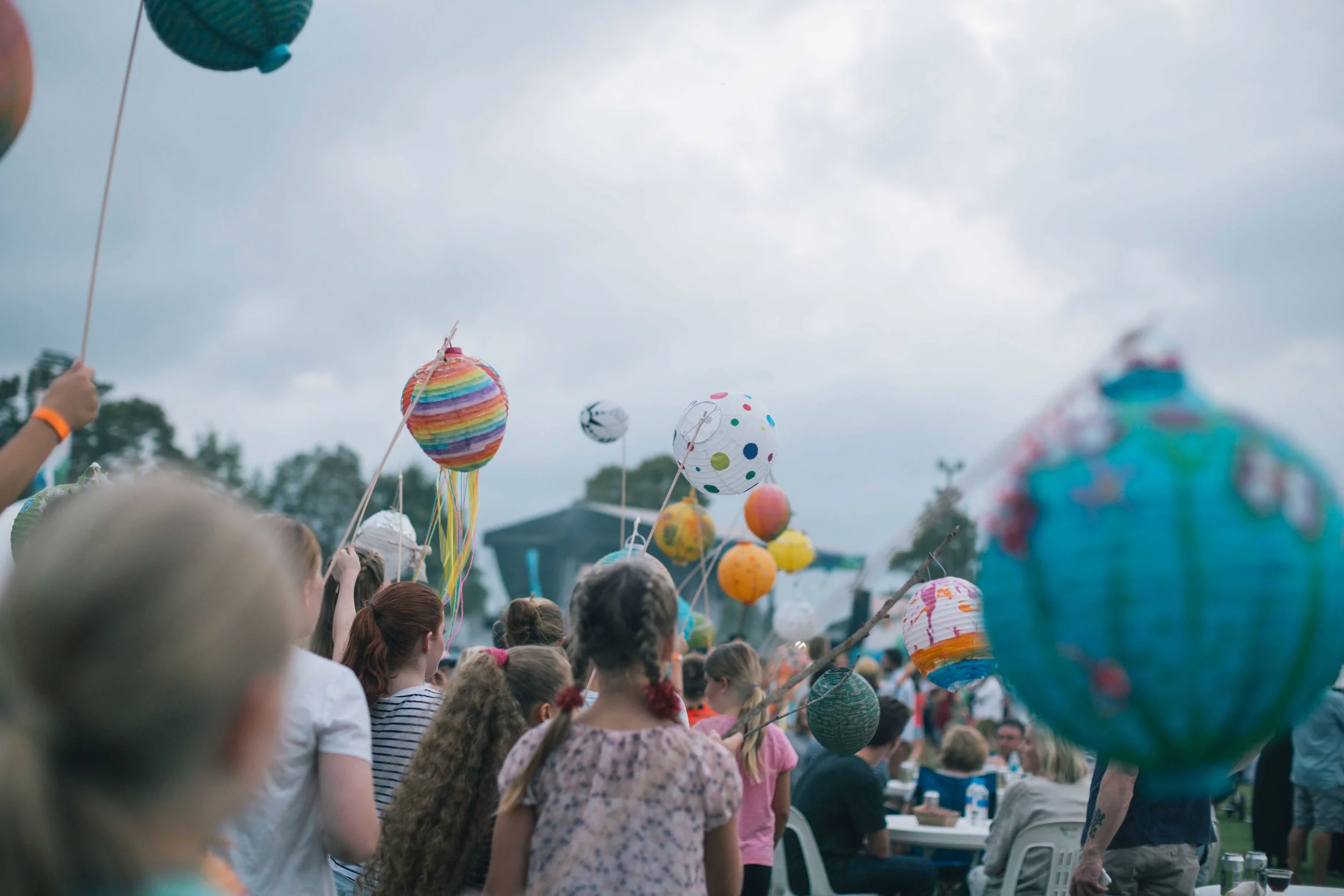 Children holding colorful paper lanterns on sticks at an outdoor event.