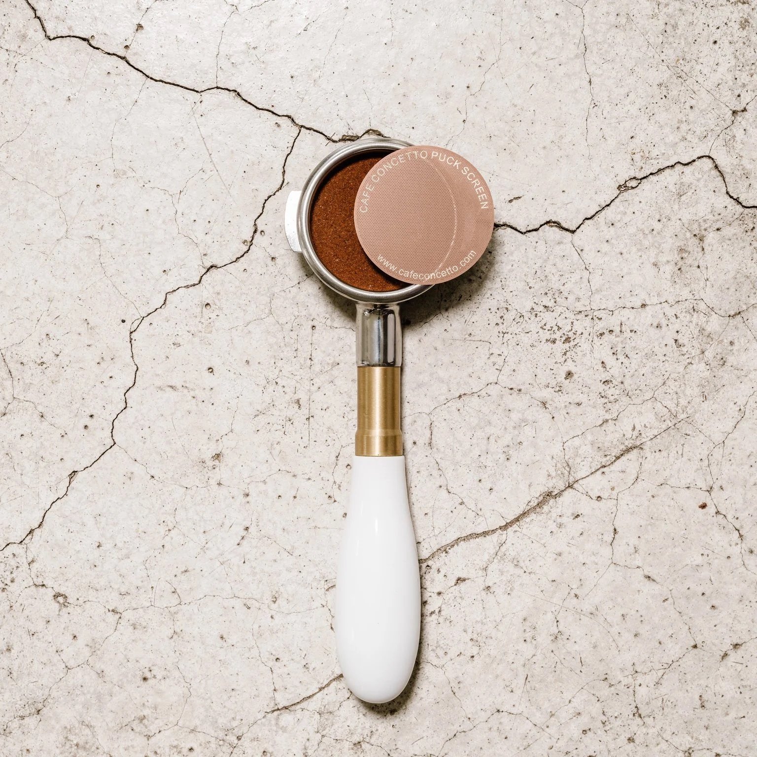 Top down view of a white handled portafilter from an espresso machine against a concrete backdrop
