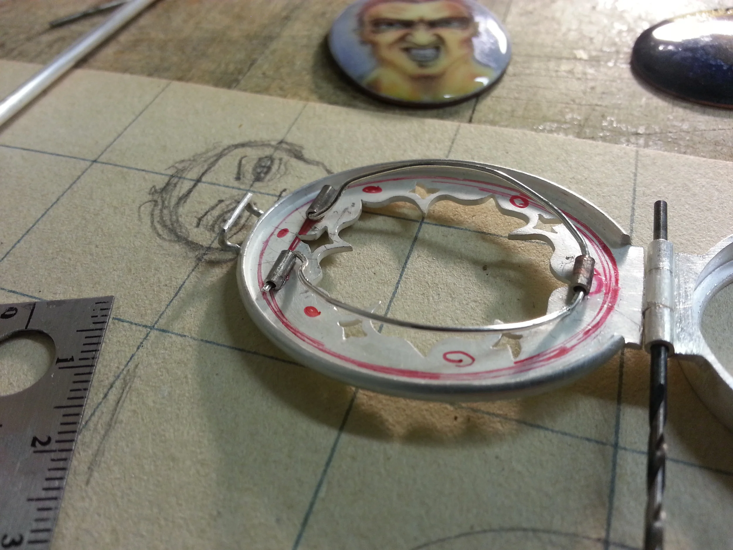 During construction; the open back reduces weight and reveals the inscription on the enamel back. For reference: the ruler is showing centimeters and the grid is 1x1 inch.