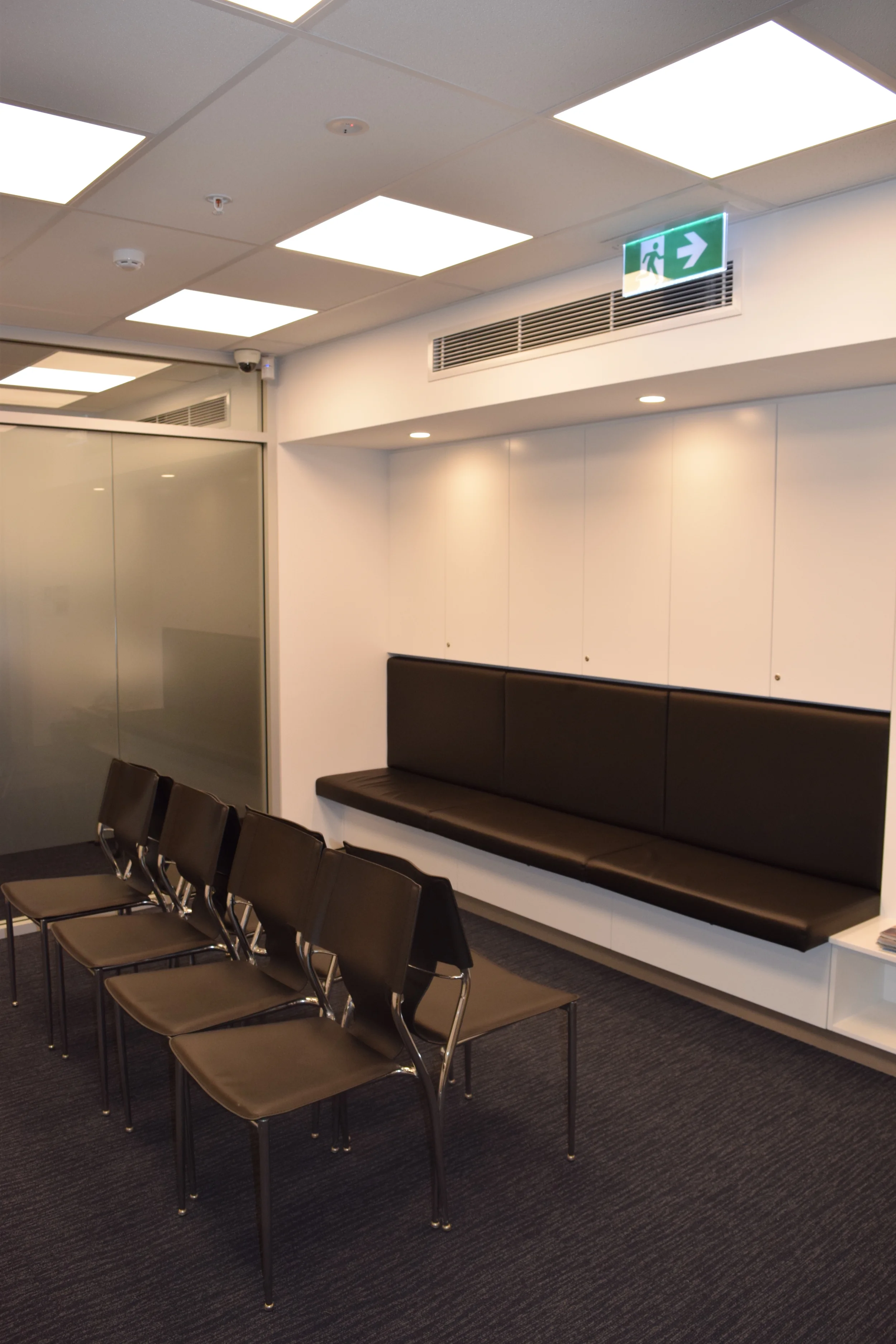  Waiting area with fixed seating and storage drawers below. Storage cupboards above seating are recessed into the wall. 