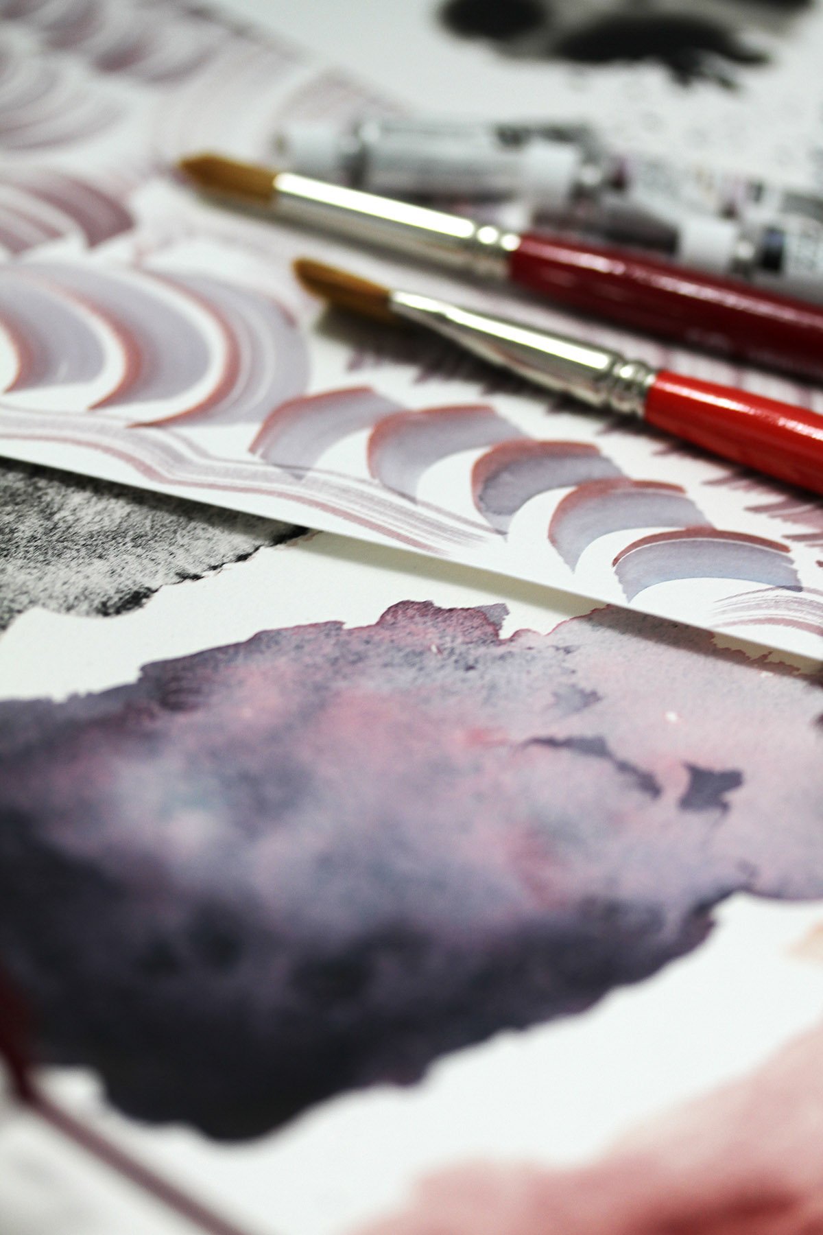 Watercolor brushstroke practice with red and violet hues, brushes in frame