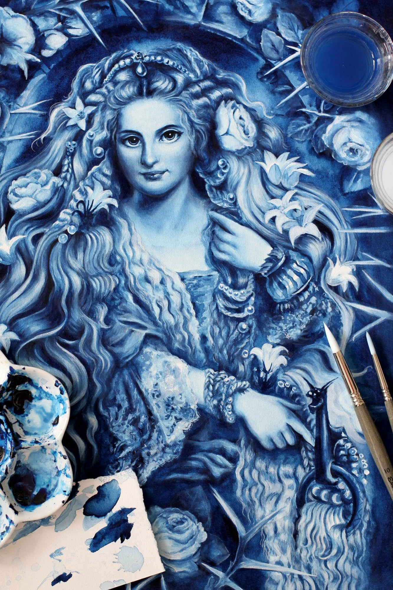 Painting process photo of Anna Sokolova’s Romance of the Rose, showing the finished blue-and-white artwork with brushes, blue pigments and watercolor materials.
