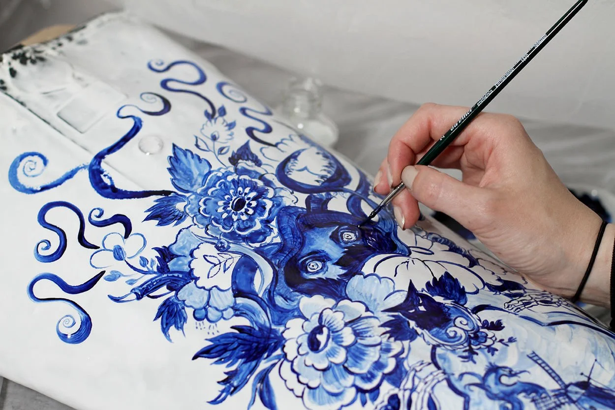 Anna Sokolova hand-painting Maison Margiela Artisanal waders with Contemporary Delft Blue illustration, creating a couture piece inspired by blue-and-white ceramics and narrative art.