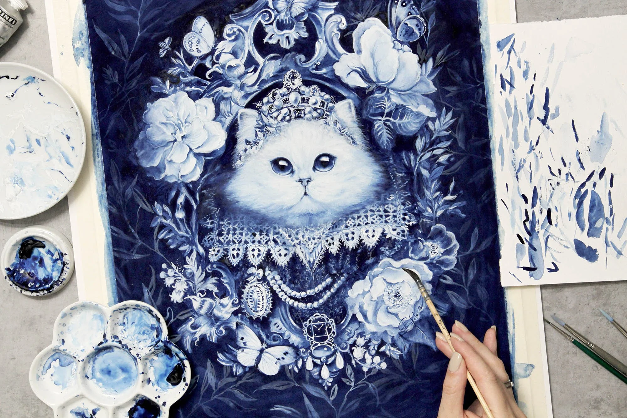 The White Cat by Anna Sokolova, contemporary Delft Blue magical realism artwork inspired by La Chatte Blanche, shown in the artist's studio with watercolor palettes, brushes and floral ornamentation during creation.
