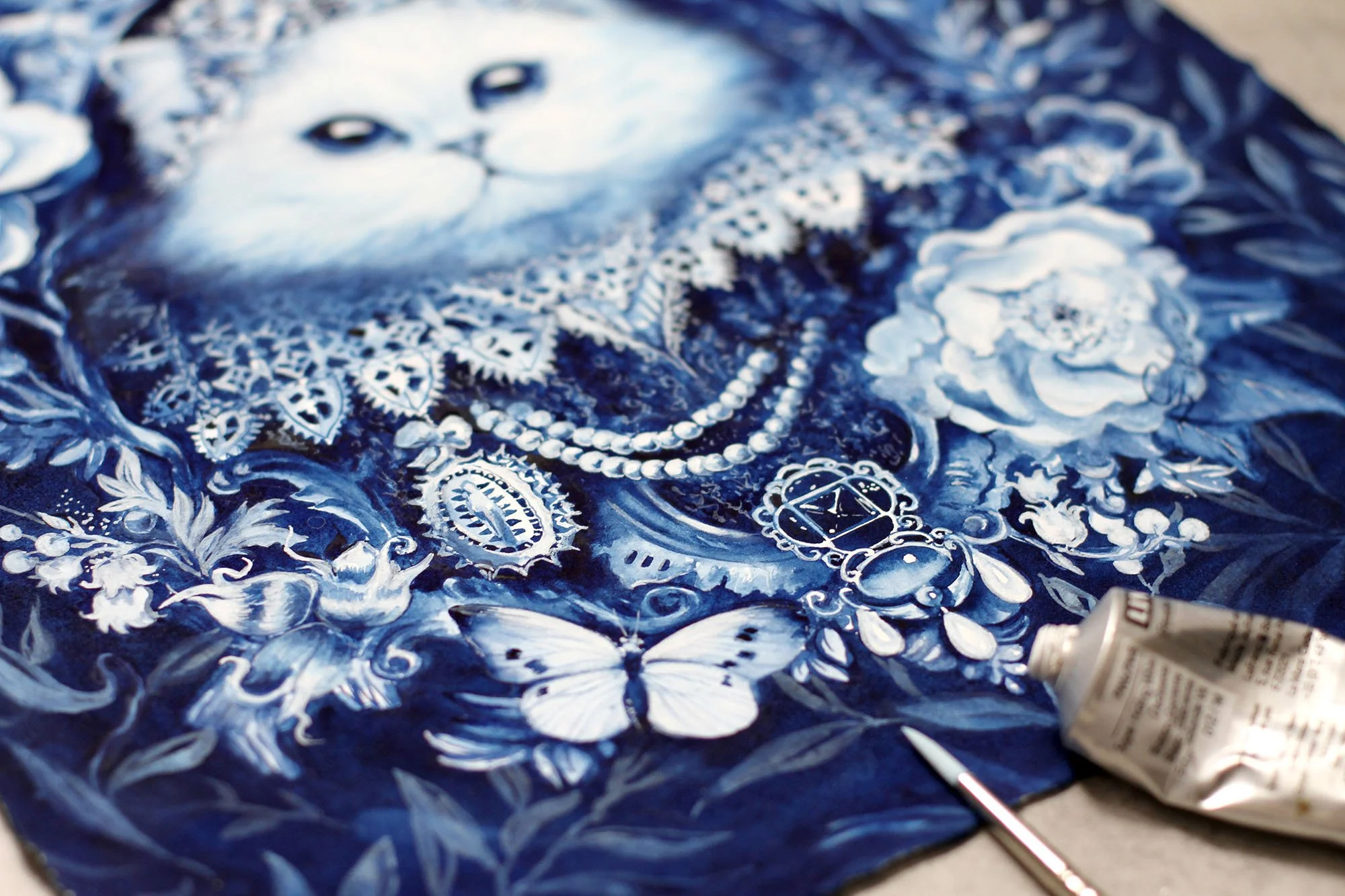Studio detail of The White Cat by Anna Sokolova, showing intricate Delft Blue brushwork, floral ornamentation, butterflies and painting materials during the creation process.