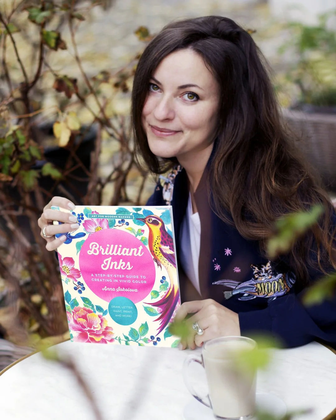 Portrait of artist and author Anna Sokolova holding her book Brilliant Inks at an outdoor café.