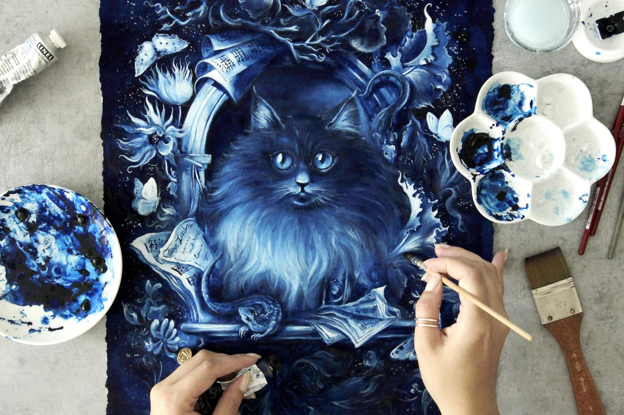 Studio view of Tomcat Murr by Anna Sokolova, a contemporary Delft Blue painting inspired by E.T.A. Hoffmann's literary cat, shown alongside palettes, brushes and mixed-media materials.