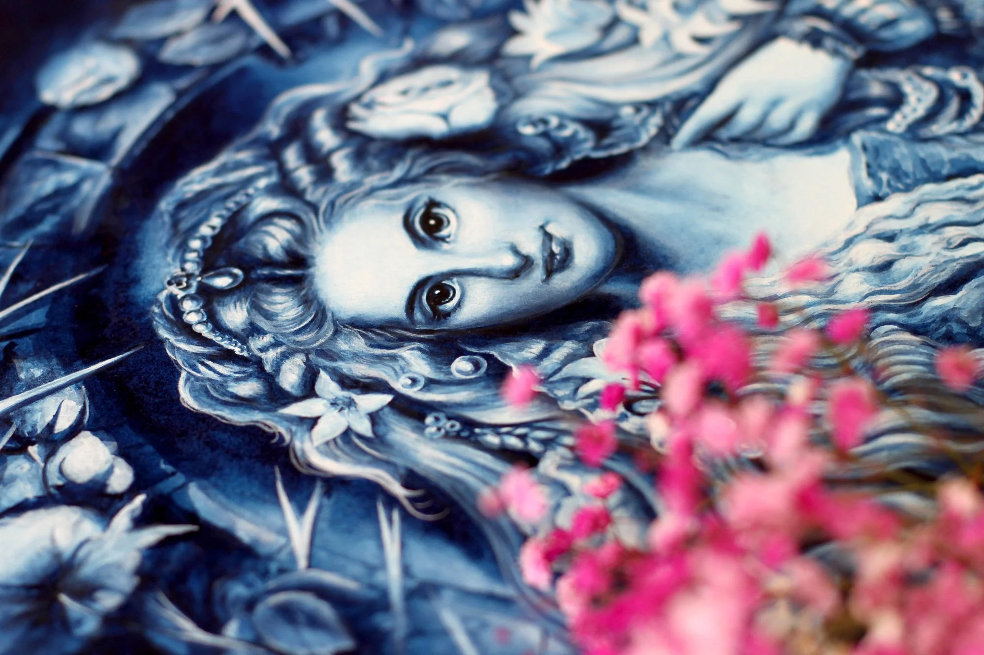 Process photo with pink flowers in foreground Process detail of Anna Sokolova’s Romance of the Rose artwork, showing a blue-and-white portrait surrounded by roses, lilies, thorny branches and pink flowers.