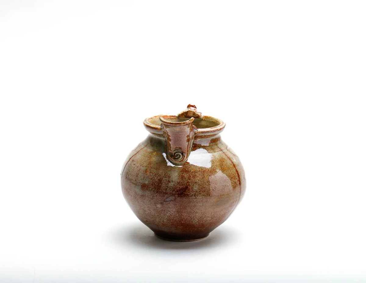 orangey-green-yellow jug with short pourer and detailed handle and decorative slip on the body of the jug