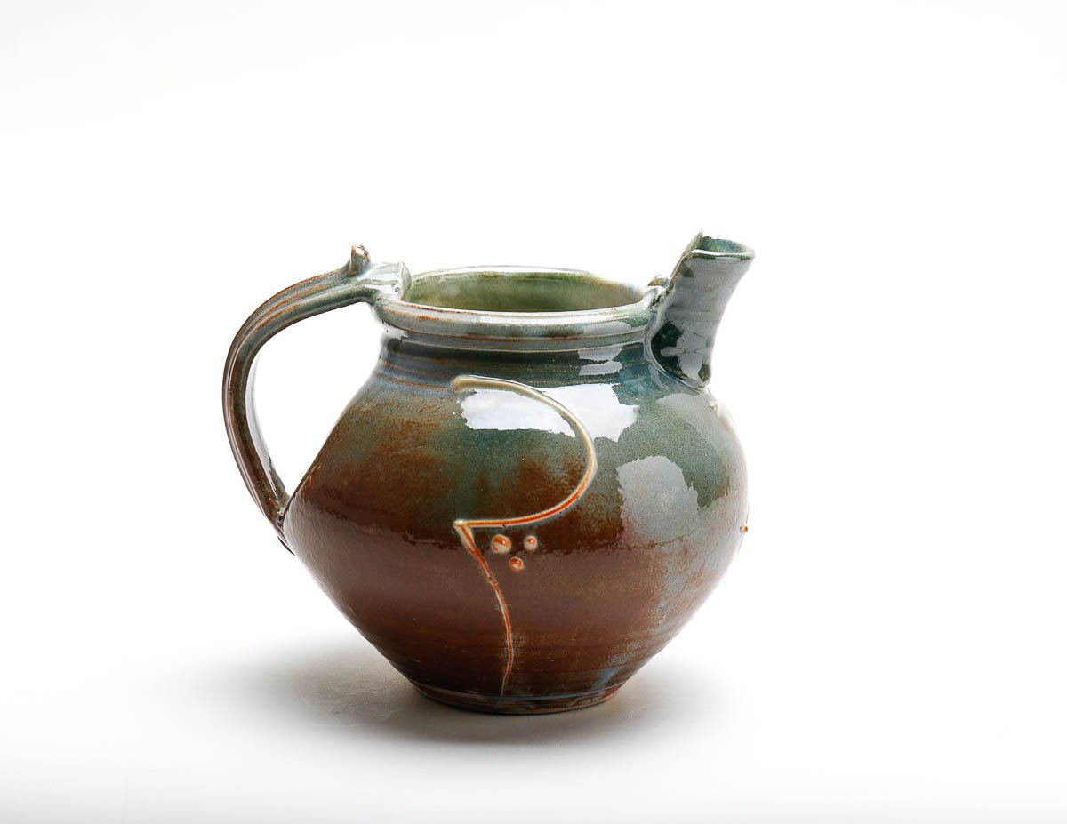 orangey-green-yellow jug with short pourer and detailed handle and decorative slip on the body of the jug