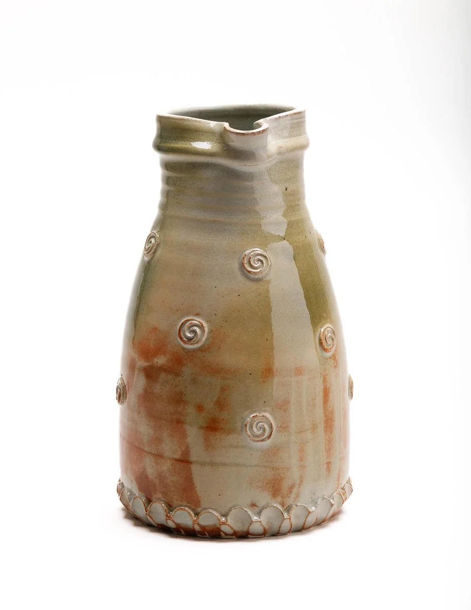 large jug in pale green glaze and orange patches, with small swirl details around the body of the jug and a detailed handle
