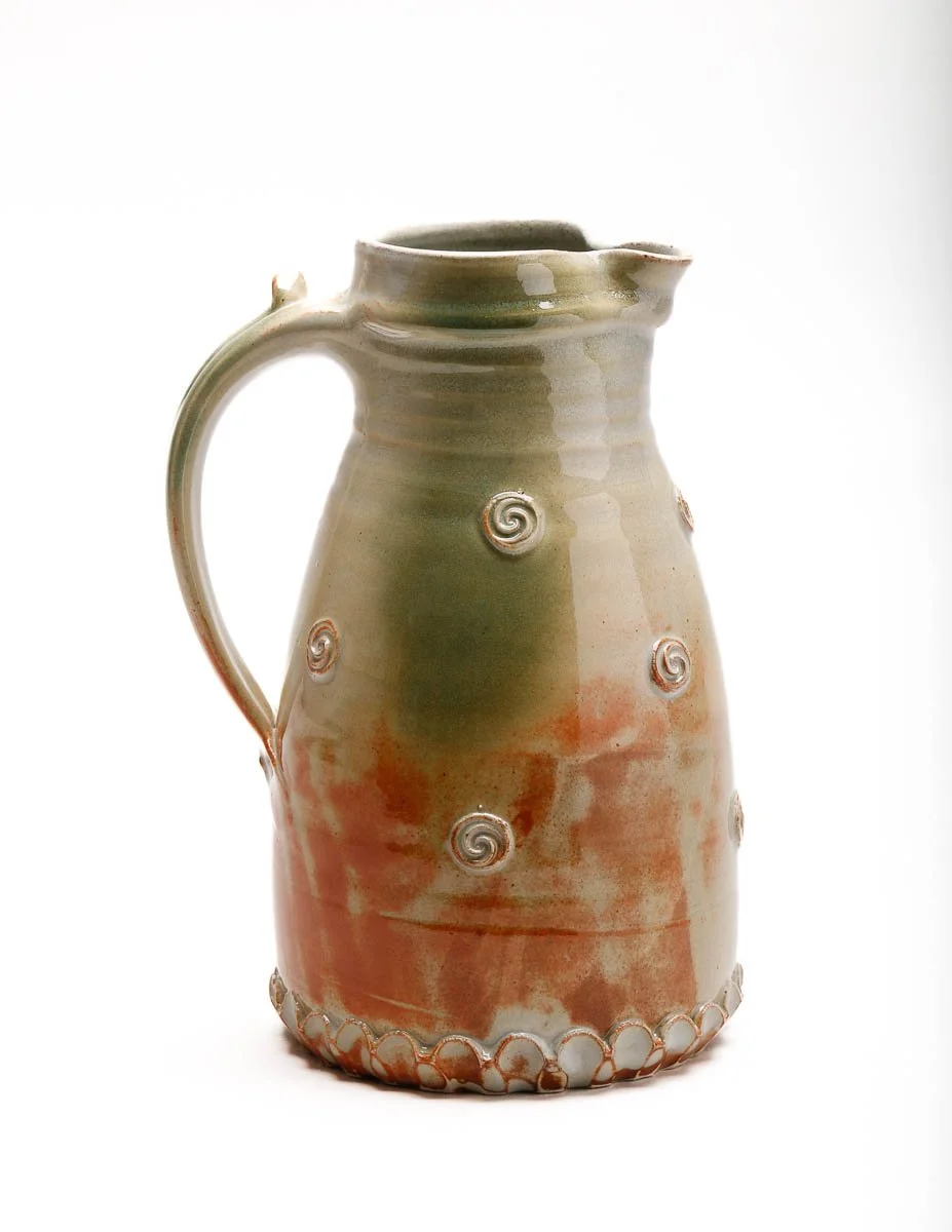 large jug in pale green glaze and orange patches, with small swirl details around the body of the jug and a detailed handle