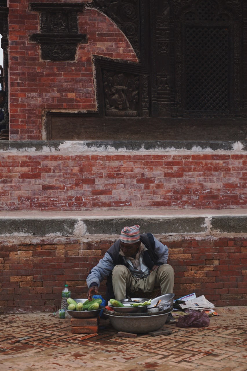  A vendor in front of one of Bhaktapur’s traditional buildings decorated with complex woodwork  