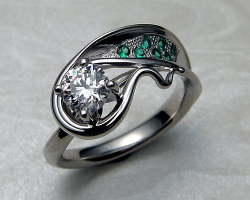 Asymmetrical, free-form, engagement ring, with diamond and emeralds.