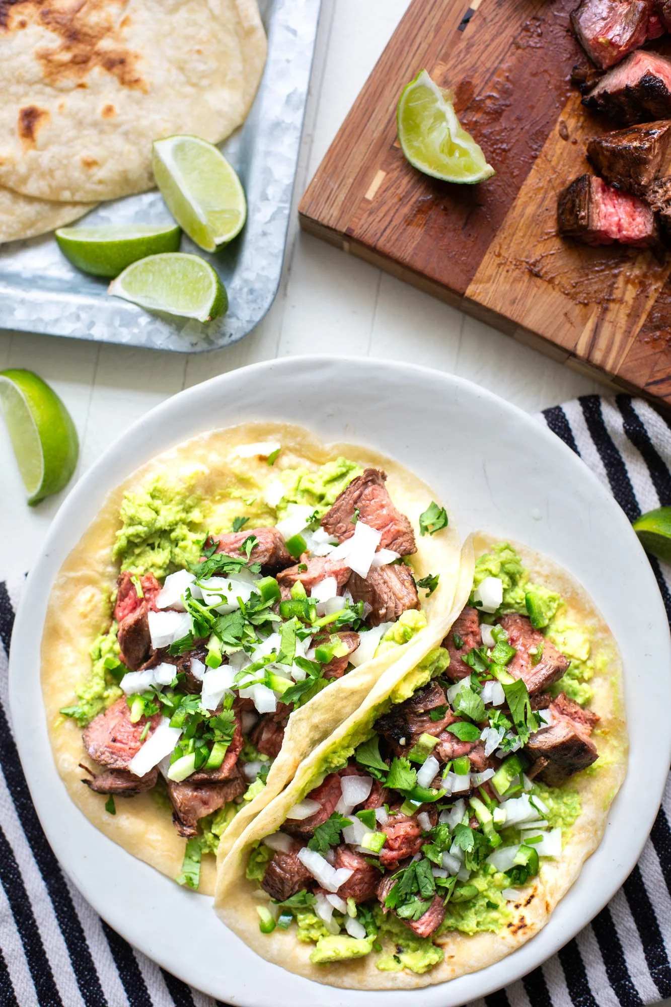 Carne Asada tacos served on a plate with onions, cilantro, and avocado.