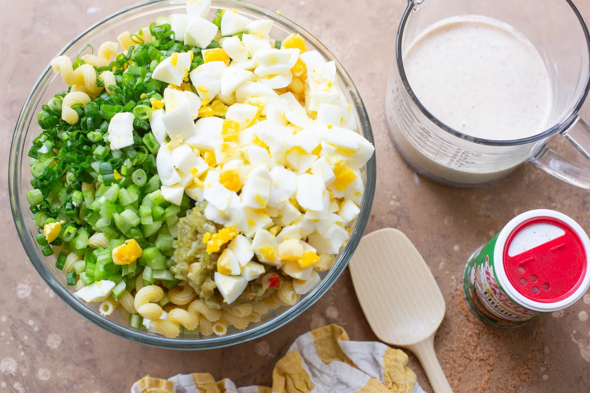 A bowl of deviled egg pasta salad ingredients and dressing on the side about to get mixed.