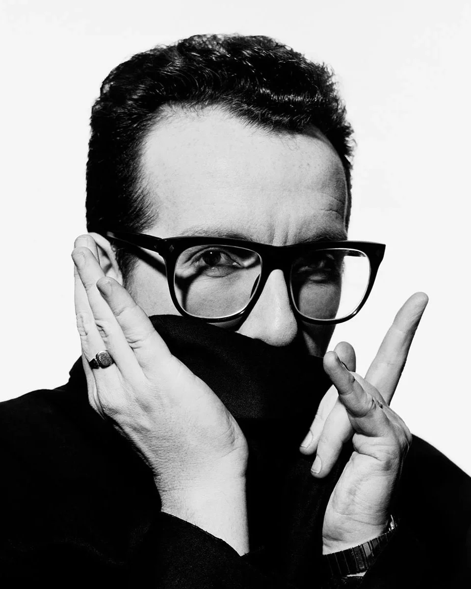 Elvis Costello pulling his shirt up to his nose